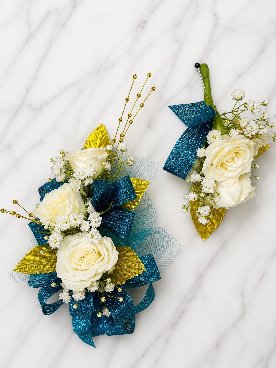 Teal Treasue Formal Set - MAGNETIC BOUTONNIERE WARNING: CONTAINS STRONG MAGNETS. DO NOT USE IF YOU HAVE A PACEMAKER, DEFIBRILLATOR, INSULIN PUMP, COCHLEAR IMPLANT, NEUROSTIMULATOR, OR OTHER IMPLANTED MEDICAL DEVICE. KEEP AWAY FROM ELECTRONICS, CREDIT CARDS, HOTEL KEY CARDS, AND CHILDREN.  Teal Treasure  Crisp white roses, vibrant teal ribbon, gold accents, and delicate filler flowers come together in Teal Treasure, a striking corsage and boutonniere collection designed for prom, homecoming, dances, banquets, weddings, and formal events. The bold teal and gold color combination creates a fresh, modern look while the white roses add timeless elegance.  Standard includes a wrist corsage with 3 spray roses and a matching magnetic boutonniere with 2 roses. Deluxe includes 4 spray roses in the corsage. Premium includes 5 spray roses for additional fullness and flower coverage. All boutonnieres include 2 roses.  Perfect for prom flowers, wrist corsages, magnetic boutonnieres, corsage and boutonniere sets, homecoming flowers, dance flowers, and formal event flowers.  Because each corsage and boutonniere is individually designed, no two sets will be exactly alike. Ribbon, filler flowers, bracelets, decorative accents, and other design elements may vary based on availability. While individual details may differ, the overall color palette, roses and/or flowers, style, and appearance of the Teal Treasure collection will be maintained.