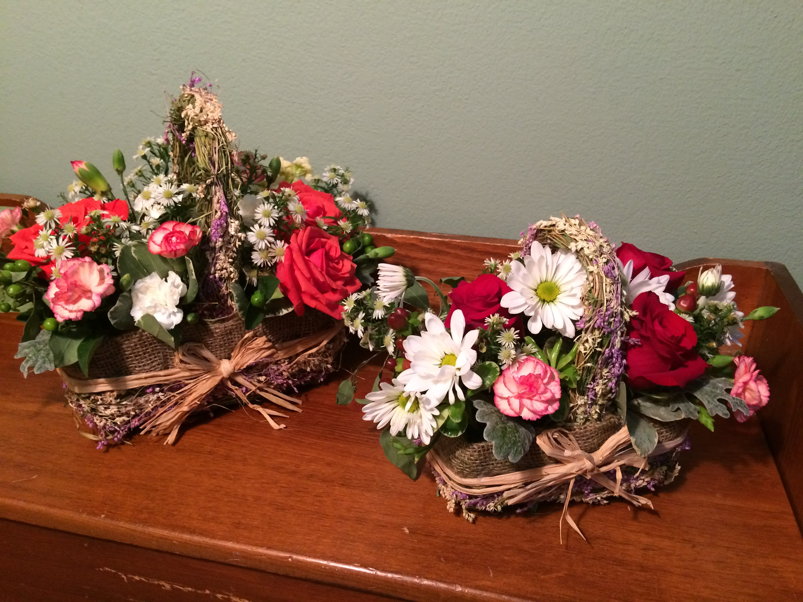 Two rustic floral baskets with red roses and white daisies