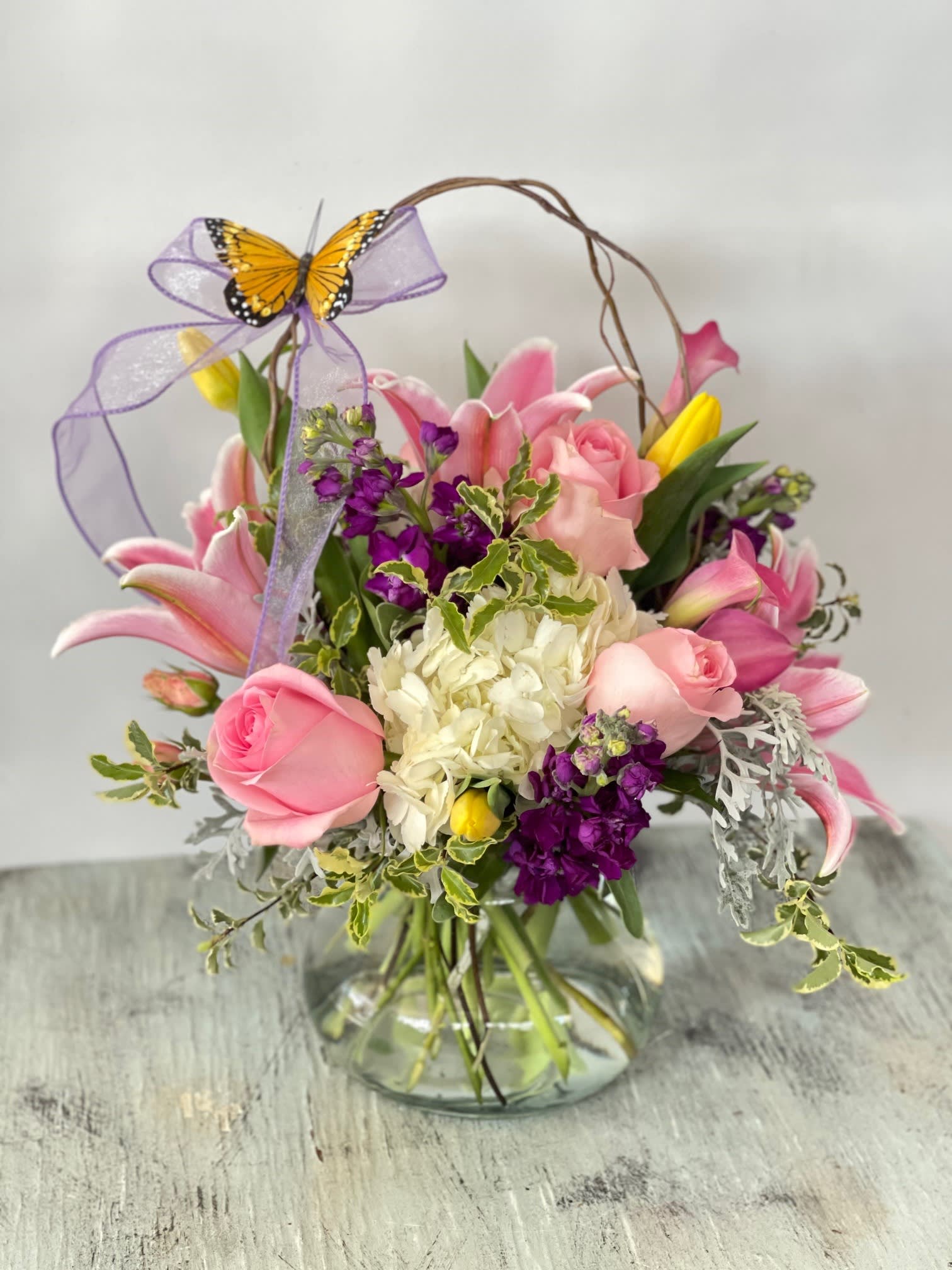 Pink and purple flower arrangement in a glass vase with a butterfly bow