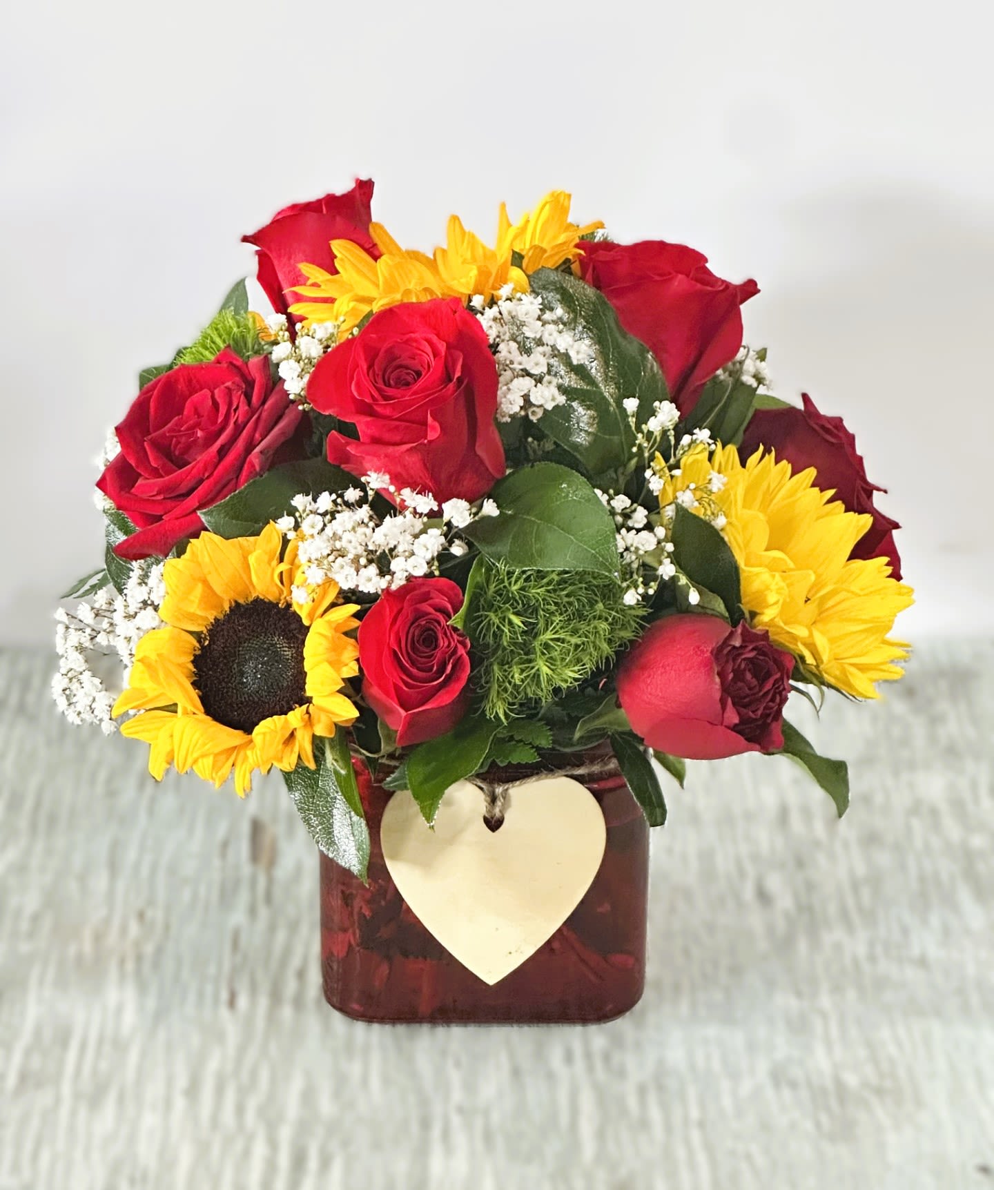 Bouquet of red roses and yellow sunflowers in a square vase with a heart tag