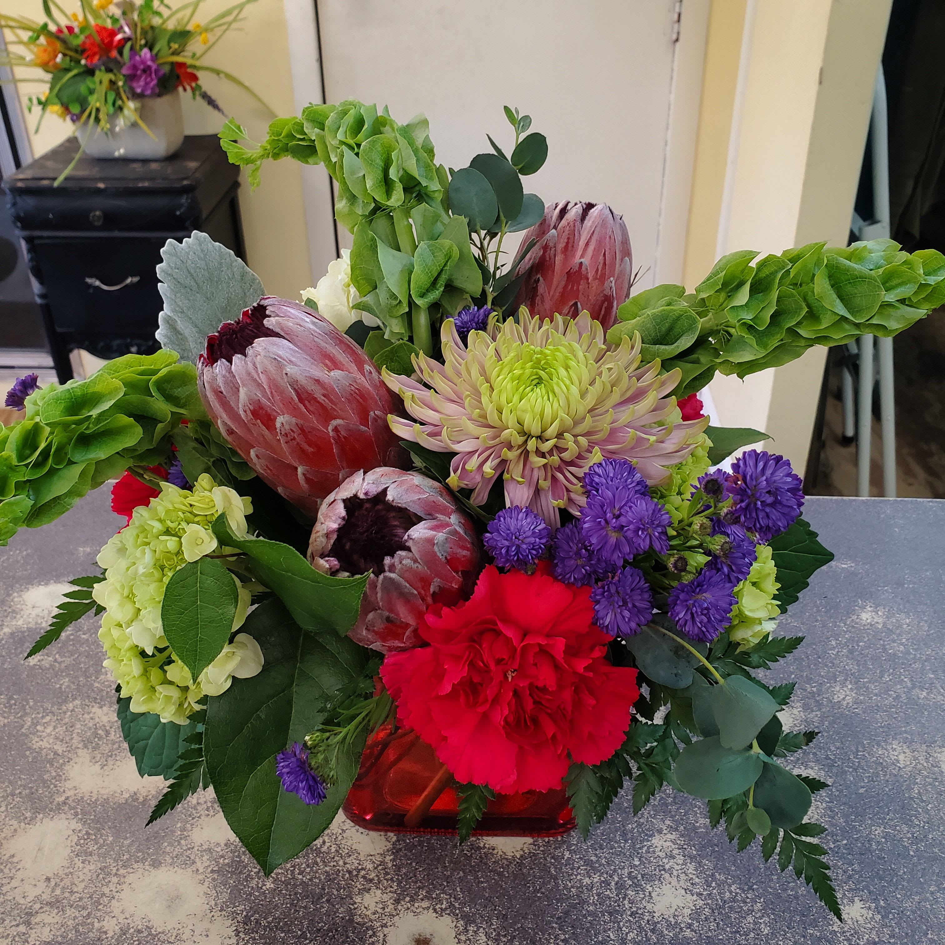 Tropical Delight  - Tropical arrangement filled with pink protea and accented with bells of Ireland and complimentary foliage.  Low compact design 