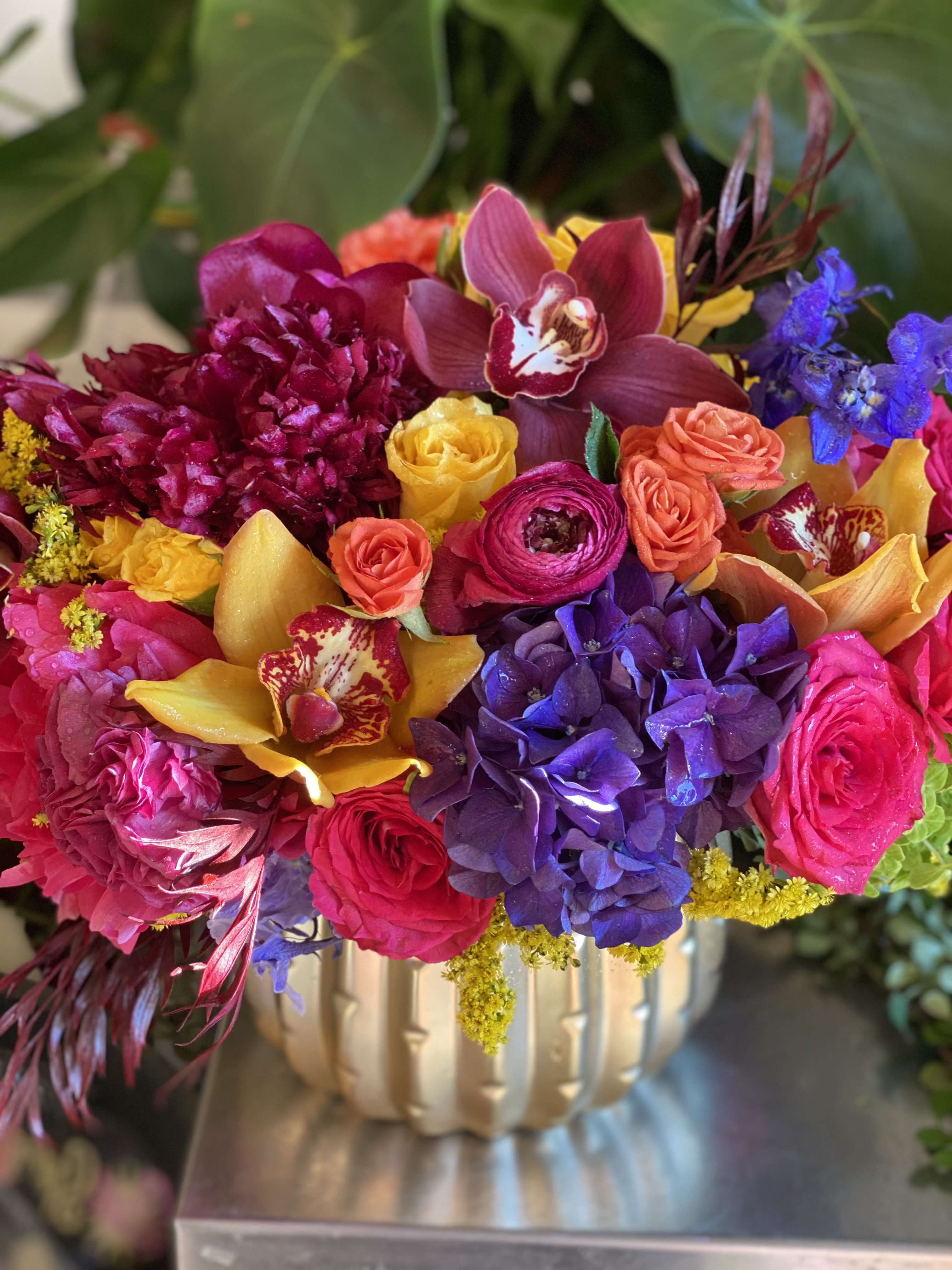 Colorful bouquet in a gold vase with orchids, roses, hydrangeas, and ranunculus