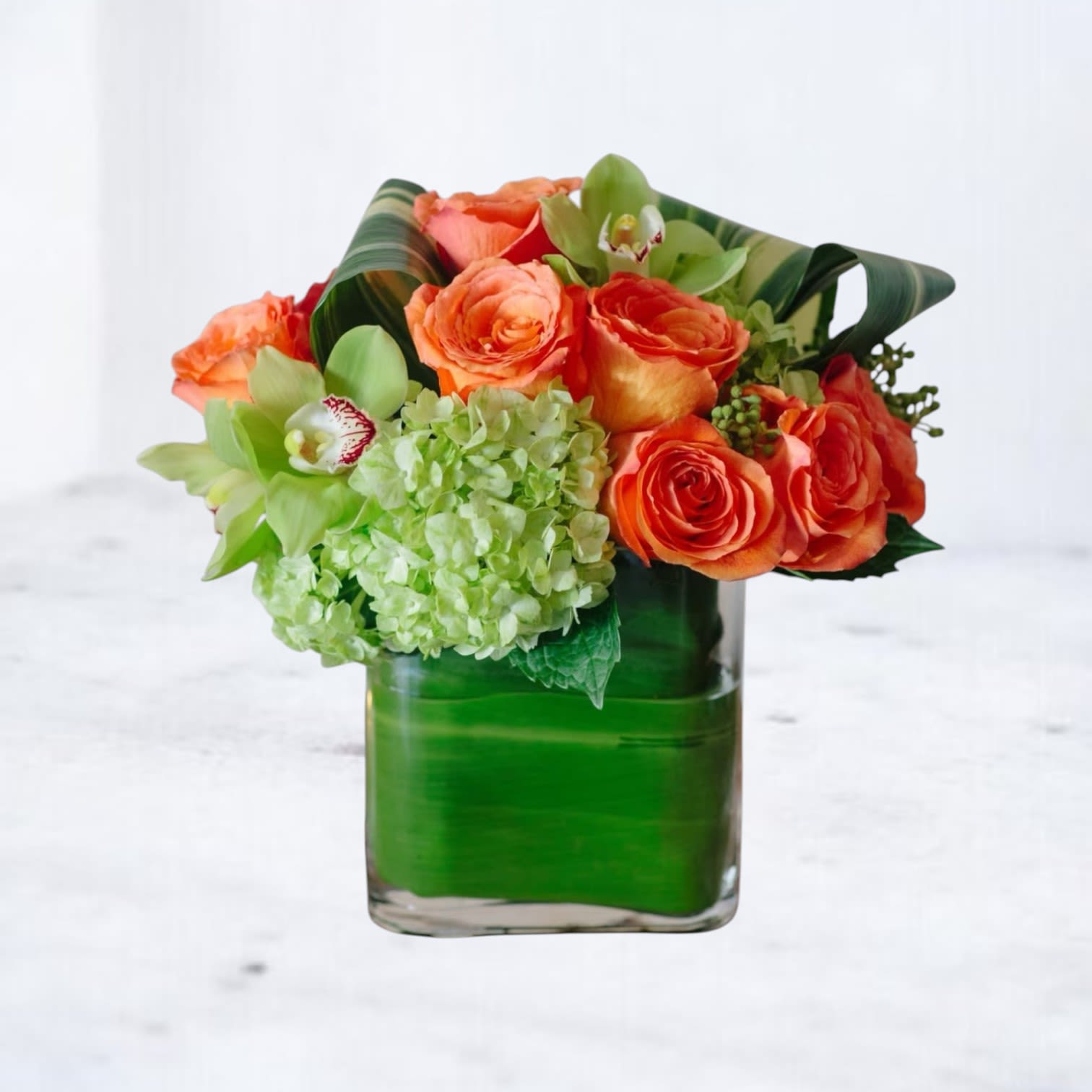 Citrus Radiance - Add a vibrant splash of joy to any room with Citrus Radiance, a bold and modern flower arrangement designed to energize the senses. Featuring vivid orange roses, lush green hydrangeas, and striking green cymbidium orchids, this eye-catching bouquet is a celebration of color, texture, and contemporary style.  Perfect for birthday flowers, congratulatory gifts, thank-you surprises, or simply brightening someone’s day, Citrus Radiance makes a stunning statement for any occasion. Arranged in a sleek glass vase, it's a show-stopping piece that brings life and cheer wherever it’s placed. 