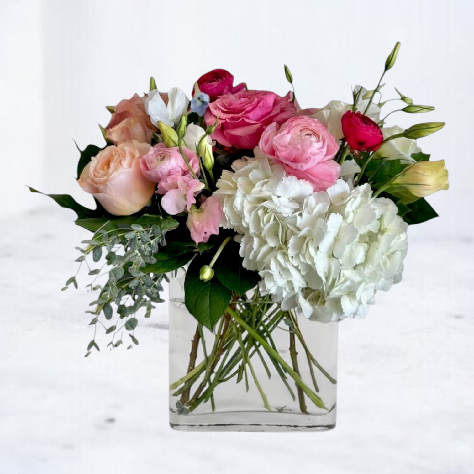 Bellini - Bellini is a romantic garden-style floral arrangement featuring blush roses, pink ranunculus, white hydrangea, lisianthus, and seasonal blooms artfully arranged in a clear glass vase. Inspired by the soft hues of its namesake cocktail, Bellini blends delicate pinks, creamy whites, and lush greenery into a design that feels effortlessly elegant.  Perfect for birthdays, anniversaries, new babies, thank you gifts, sympathy gestures, or simply brightening someone's day, Bellini offers timeless beauty with a fresh, modern touch. Its airy garden styling and soft color palette create a graceful arrangement that feels both sophisticated and inviting.  Handcrafted with premium seasonal flowers, every Bellini arrangement is uniquely beautiful and designed to leave a lasting impression.  Available for flower delivery throughout Magnolia, Montgomery, The Woodlands, Conroe, Spring, Tomball, and surrounding Houston communities.