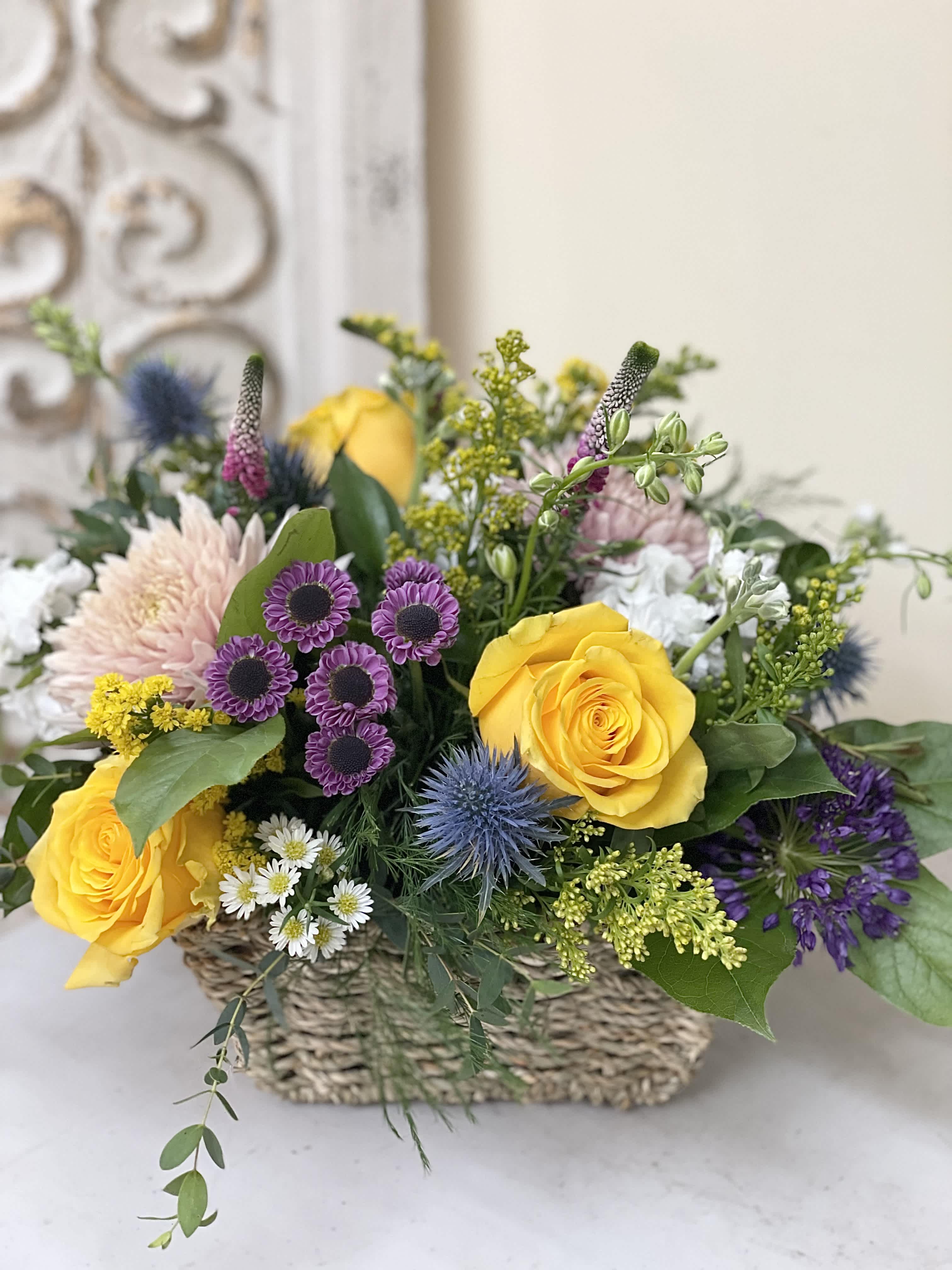 Mixed flower arrangement in a woven basket with yellow roses and purple blooms