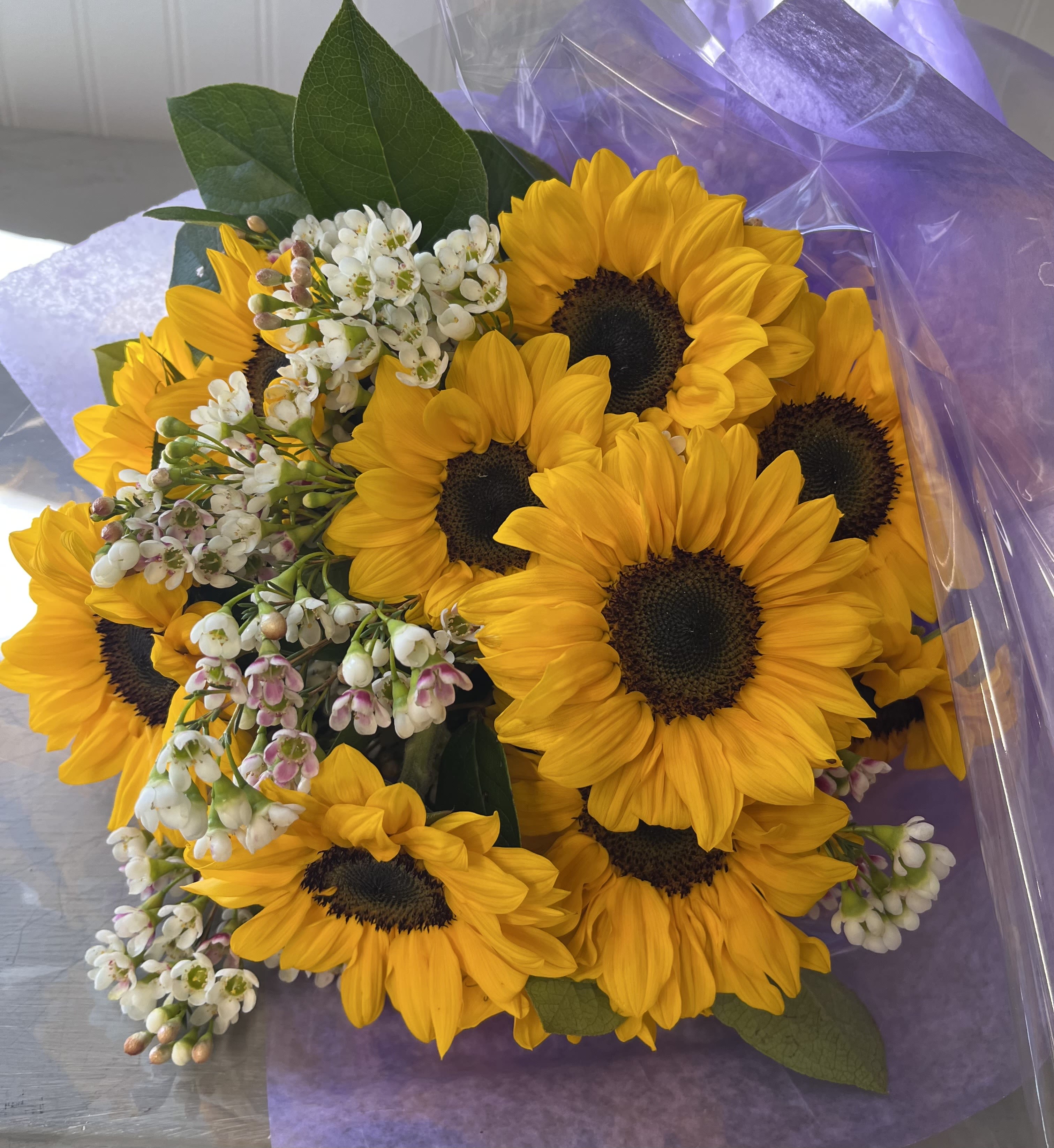 Bouquet of yellow sunflowers with small white blossoms wrapped in purple paper
