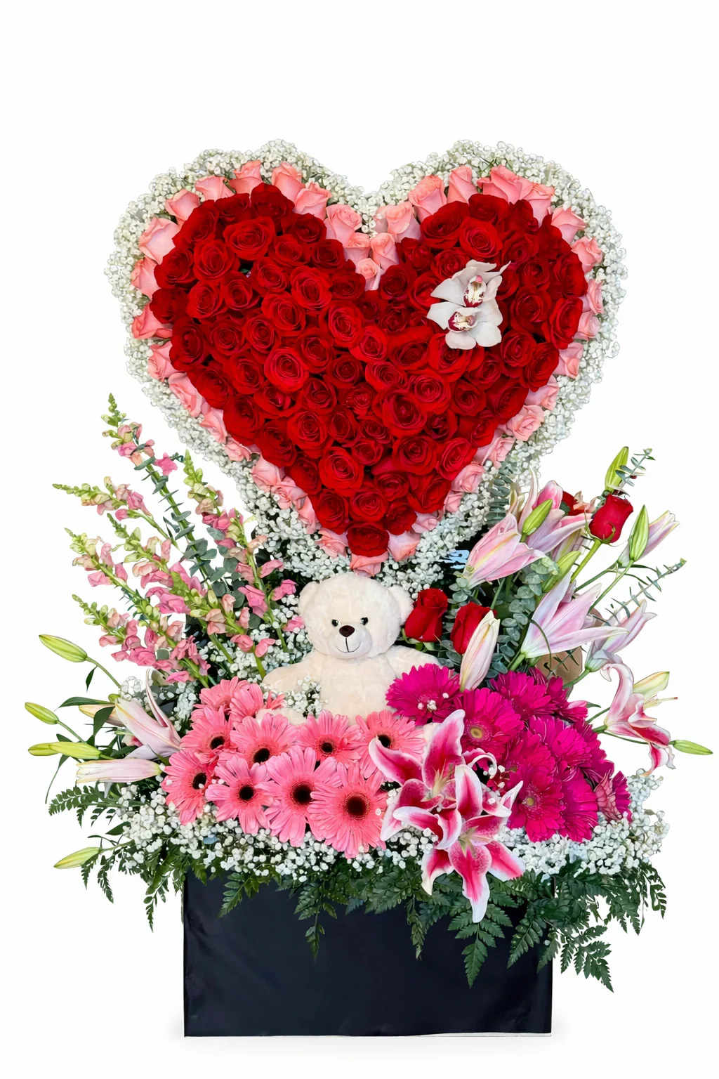 Arreglo de Corazon - El corazón estructural está montado sobre una base de jardín exuberante y rebosante, que presenta un vibrante contraste de gerberas en tonos rosa fuerte y rosa claro, extensos lirios Stargazer y majestuosos perritos (antirrinos) de color rosa. Anidado directamente en el centro de este jardín floral premium se encuentra un tierno oso de peluche coleccionable, que fusiona el romance clásico con un toque juguetón y sentimental. Presentado en una base rectangular negra, elegante y minimalista, este arreglo ofrece una experiencia visual inolvidable de 360 grados.