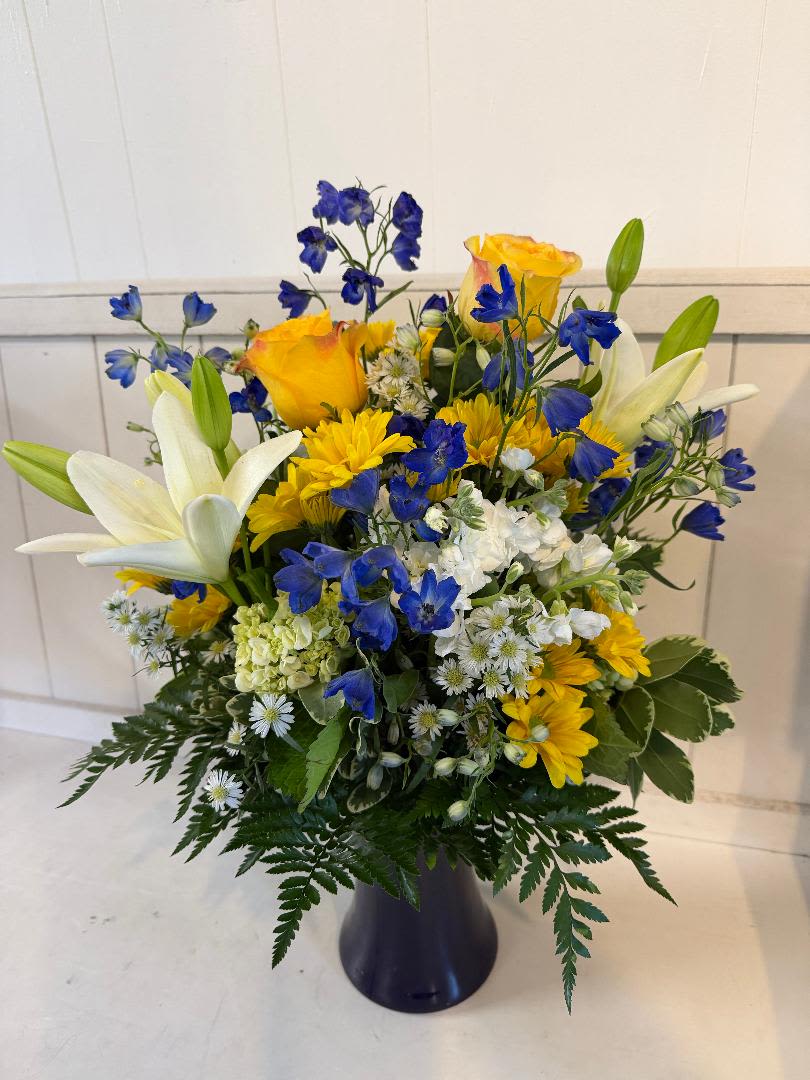 Sapphire and Sunbeams - Blue delphinium, green hydrangeas, yellow roses, yellow daisies, filler and lilies in a Cobalt blue vase 