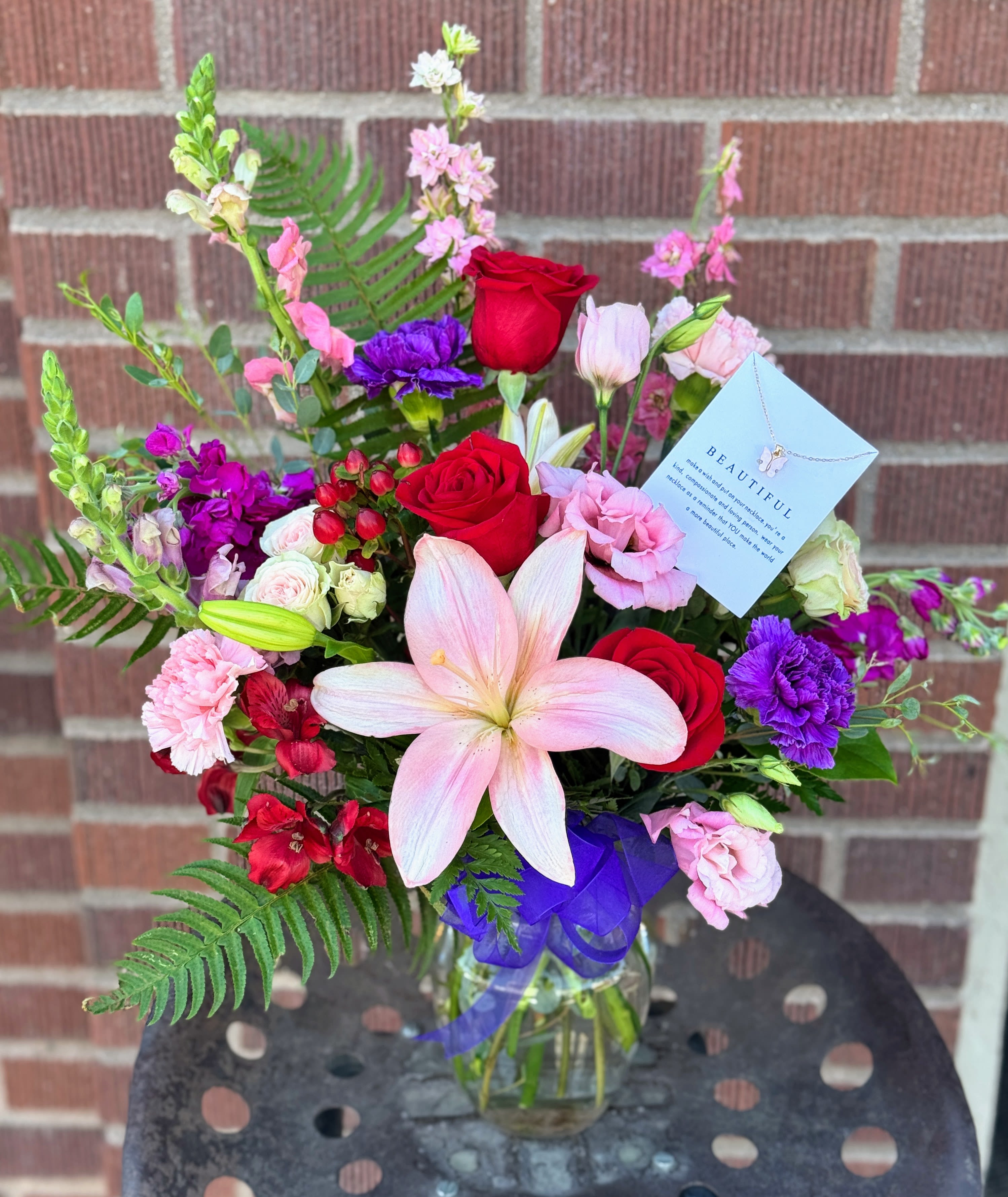 Mixed bouquet with red roses, pink lilies, and purple flowers in a glass vase