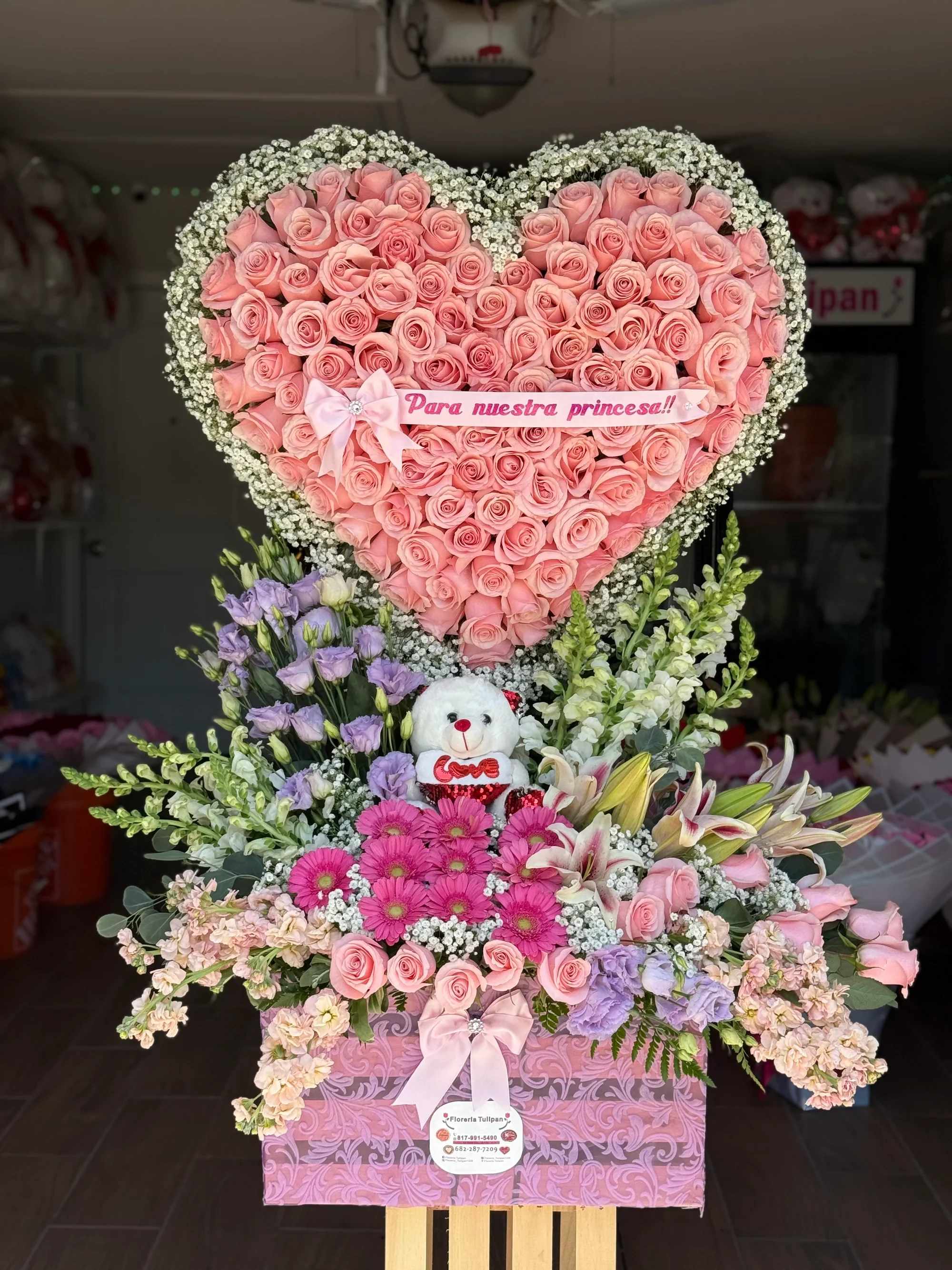 Arreglo De Dorazón de Rosas y flores surtidas 2 - Un diseño espectacular y lleno de ternura, creado para celebrar a esa persona tan especial que ilumina tu vida. Este impresionante arreglo presenta un gran corazón de rosas rosadas, rodeado de delicadas flores blancas y complementado con una base floral elegante y abundante.  Incluye:   Gran corazón elaborado con rosas rosadas premium  Marco de delicadas flores blancas (baby’s breath)  Base con variedad de flores frescas: gerberas, lirios, rosas y follaje fino  Tierno osito decorativo  Moños elegantes en tono rosa  Banda personalizada con el mensaje “Para nuestra princesa”  Ideal para cumpleaños, celebración de quinceañera, nacimiento, aniversario o para consentir a tu princesa con un detalle inolvidable.   Diseño exclusivo de gran tamaño y presentación impactante.  Disponible para entrega especial.