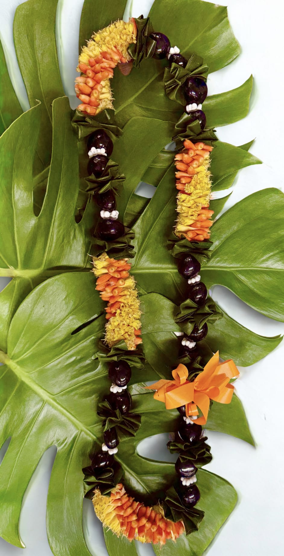 Two floral leis with orange and yellow flowers on large green leaves.