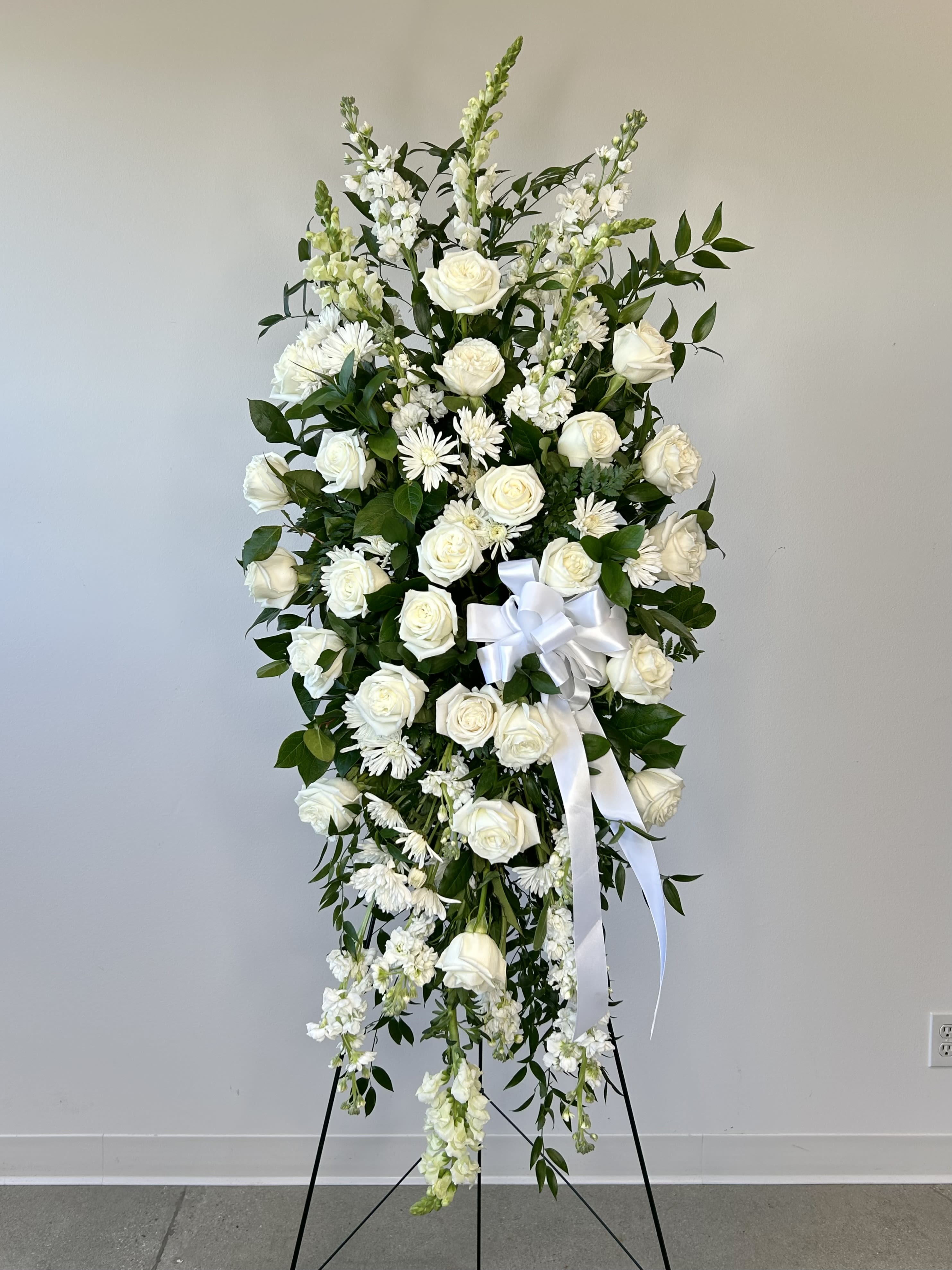 White floral standing spray with roses and ribbon on an easel