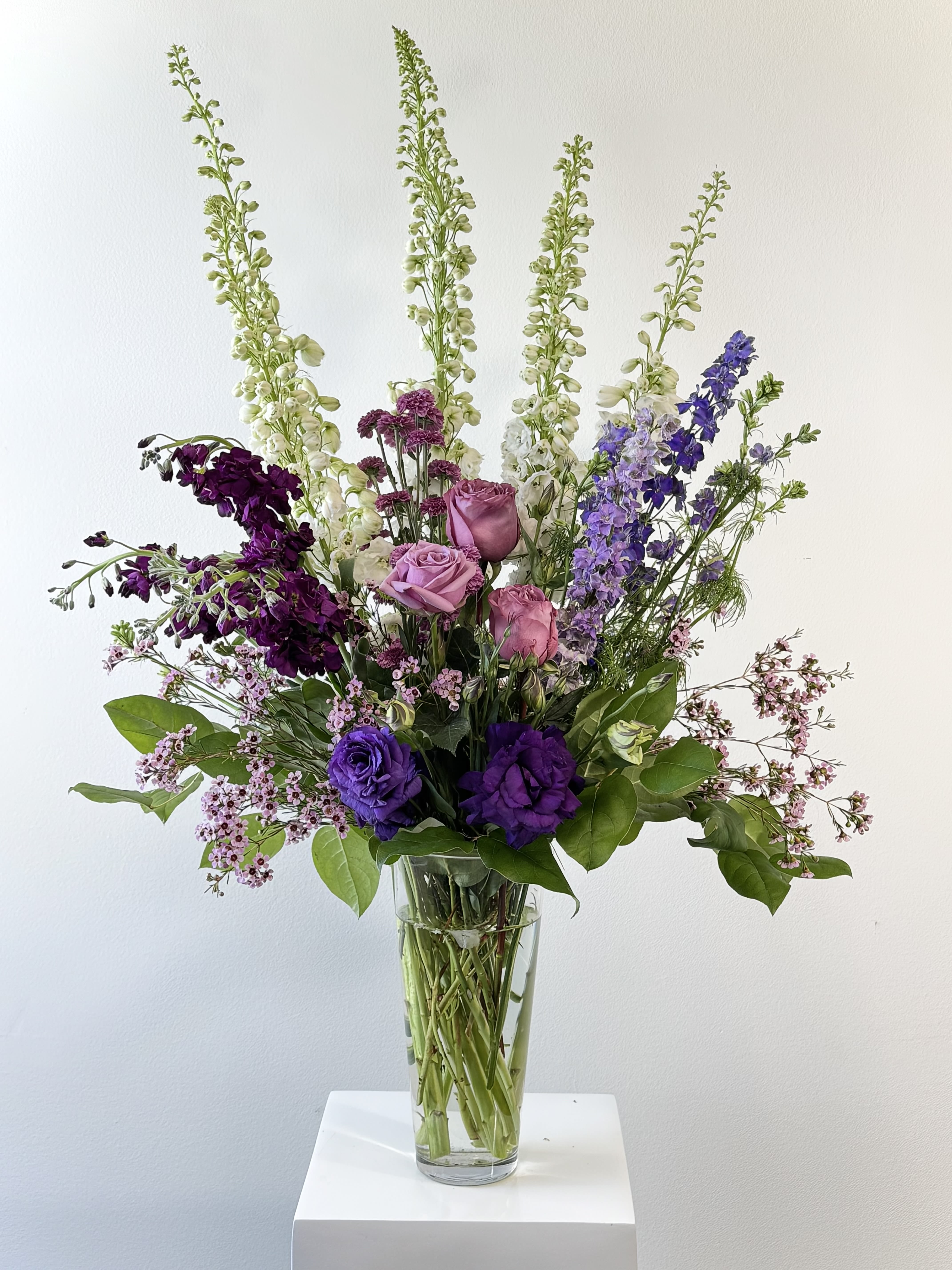 Tall mixed bouquet of purple, pink, and white flowers in a clear glass vase
