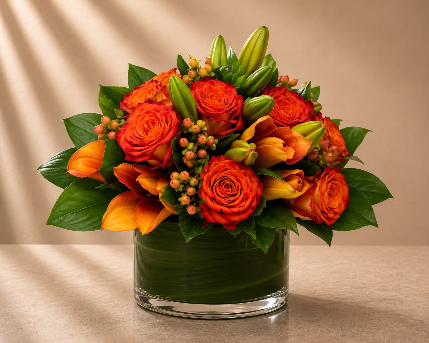 Ember Luxe - Vibrant, rich, and undeniably sophisticated, Ember Luxe is a bold designer arrangement featuring fiery orange roses, warm-toned calla lilies, hypericum berries, and lush greenery arranged in a sleek modern glass cylinder vase.  The glowing sunset palette creates a luxurious statement filled with warmth, passion, and contemporary elegance. The layered textures of roses and calla lilies bring depth and movement, while the glossy foliage keeps the design polished and upscale.  This arrangement feels dramatic yet refined — perfect for clients looking for a modern luxury floral piece with rich autumn-inspired tones year-round.