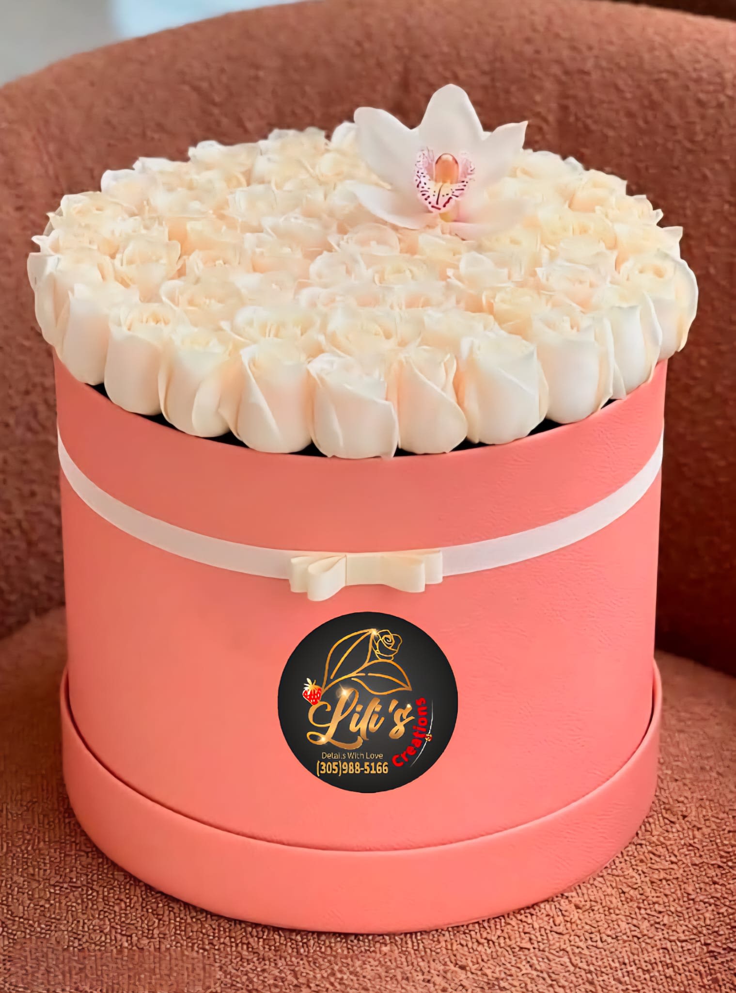 Round pink hatbox filled with white roses and a white orchid