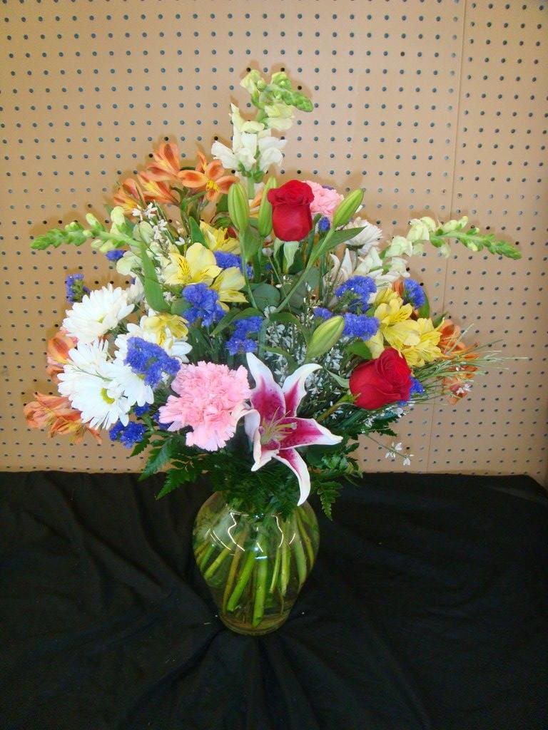 Mixed bouquet of lilies, roses, daisies, and carnations in a glass vase