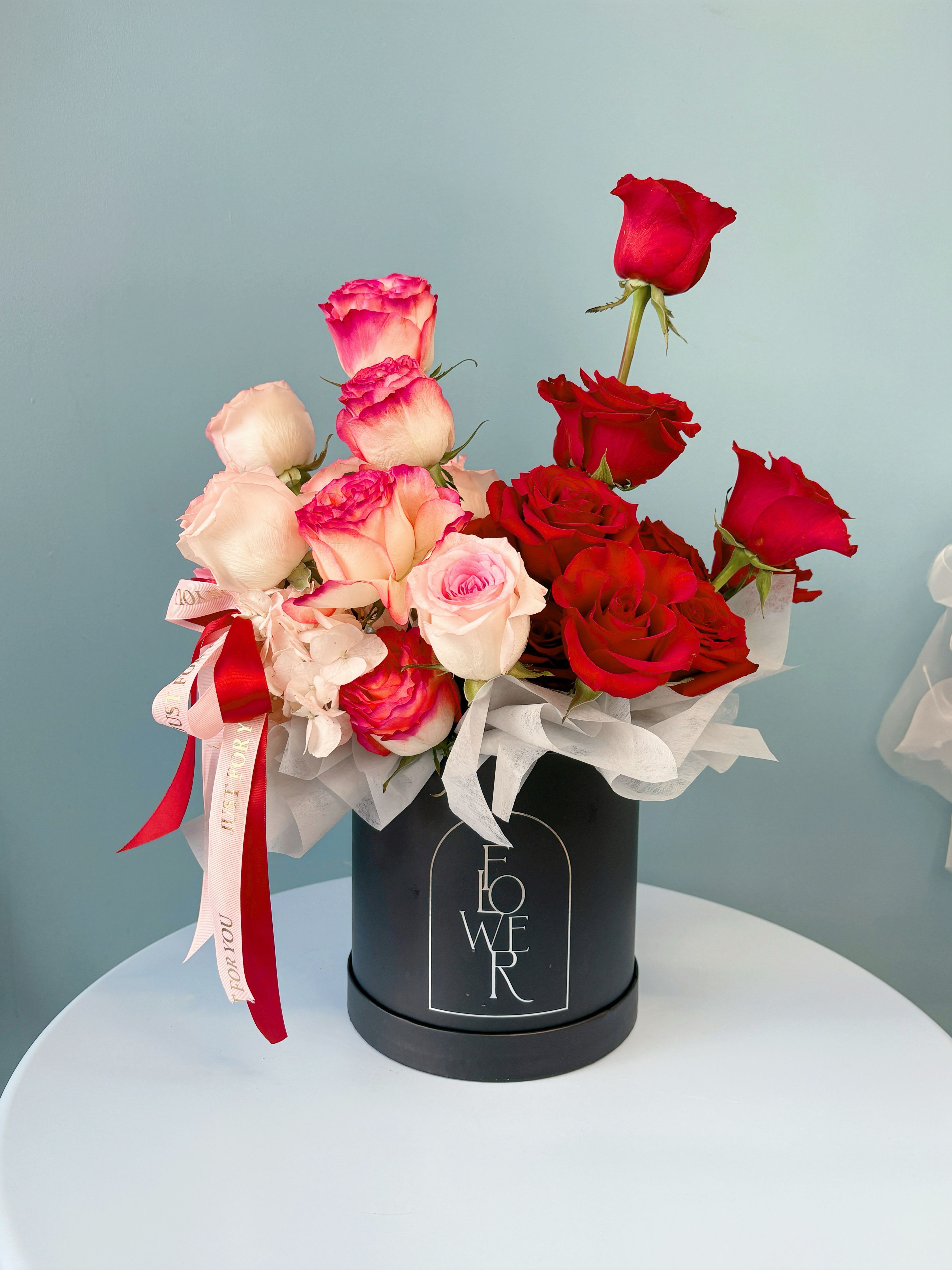 Red and blush roses arranged in a black hat box with ribbon