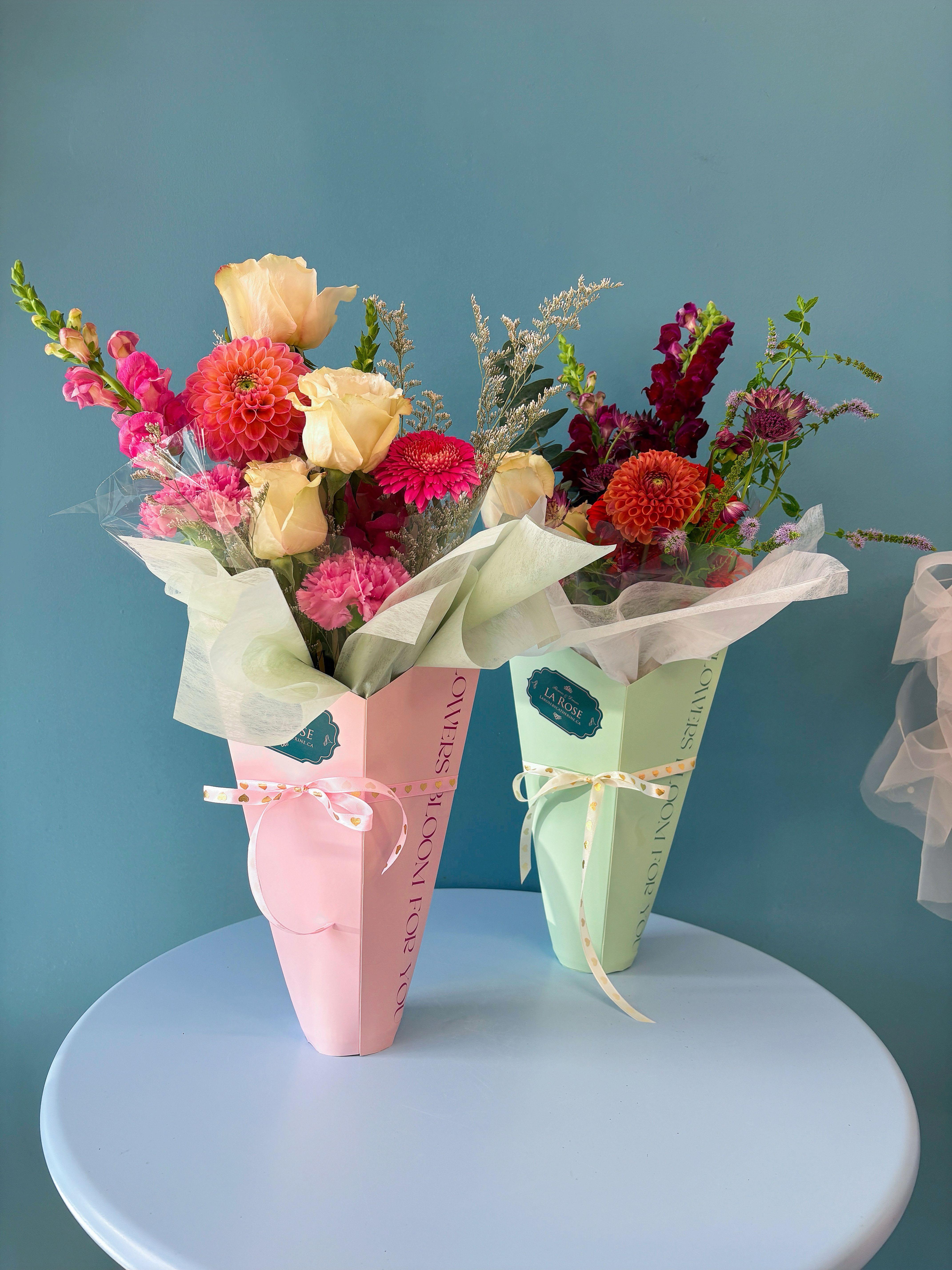 Two wrapped bouquets with pink, cream, and orange flowers in pastel boxes