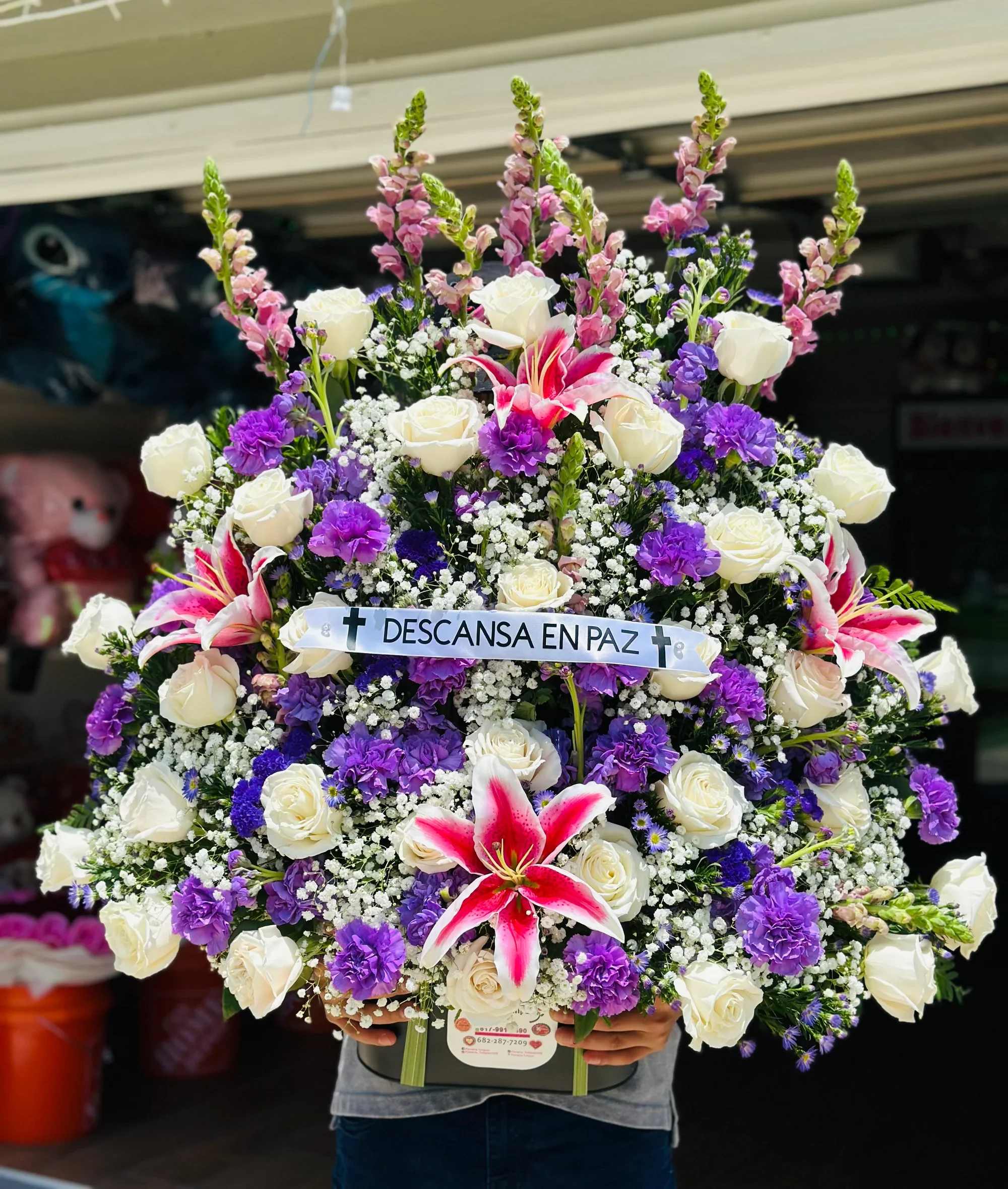 Arreglo funeral -  Arreglo Fúnebre “Descansa en Paz” – Blanco y Azul Elegante   Honra la memoria de tu ser querido con este majestuoso arreglo floral elaborado con flores frescas en tonos blanco y azul, una combinación que transmite paz, serenidad y esperanza.  Este diseño incluye hermosas rosas blancas, claveles azules, crisantemos, lirios y delicada flor nube (gypsophila), cuidadosamente acomodadas para crear una presentación elegante y solemne. Incluye banda con el mensaje “Descansa en Paz”, ideal para expresar tus condolencias con respeto y amor.   Características:  • Rosas blancas frescas premium • Claveles azules y crisantemos blancos • Lirios blancos elegantes • Flor nube decorativa • Follaje verde natural • Base resistente incluida • Banda con mensaje (opcional personalizable)   Ideal para:  • Servicios funerarios • Velorios • Homenajes y memoriales • Envíos directos a funeraria o domicilio  Un tributo floral imponente y lleno de significado que transmite apoyo y consuelo en momentos difíciles.  Contáctanos para personalizar el mensaje y coordinar la entrega puntual