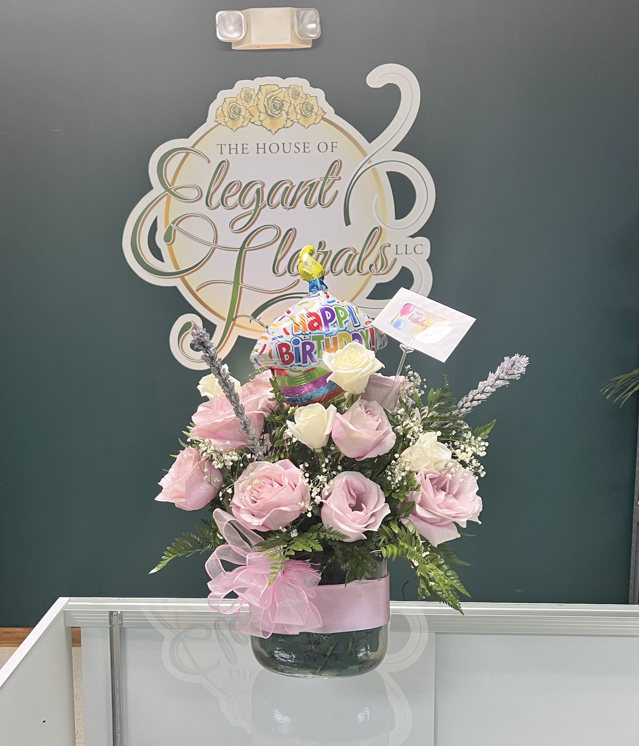 Pink and white rose arrangement in a glass vase with a birthday balloon