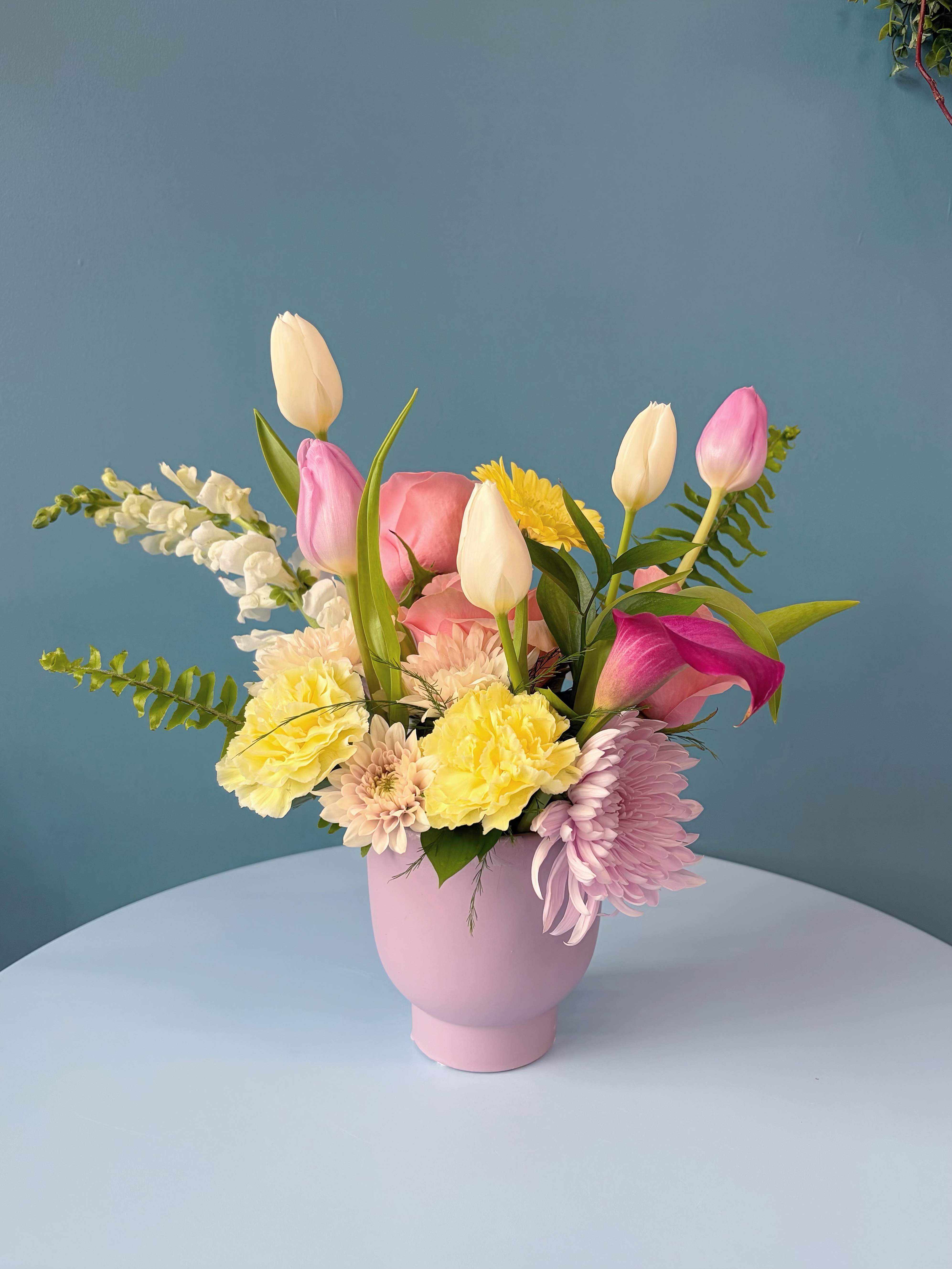 Summer Fresh Table Arrangement - Bring the joy of spring to your space with our Hello Sunshine Spring Table Arrangement, designed to capture the warmth, freshness and uplifting beauty of the season. Featuring premium seasonal blooms in soft spring tones, this arrangement blends elegant roses, cheerful gerberas and fresh textural florals with lush greenery to create a look that feels bright, airy and refined. Thoughtfully arranged in a modern vessel, it is designed to sit beautifully on dining tables, kitchen islands or as a welcoming centerpiece for any spring gathering. Fresh, joyful and effortlessly elegant — a little sunshine for your home or as a thoughtful seasonal gift.