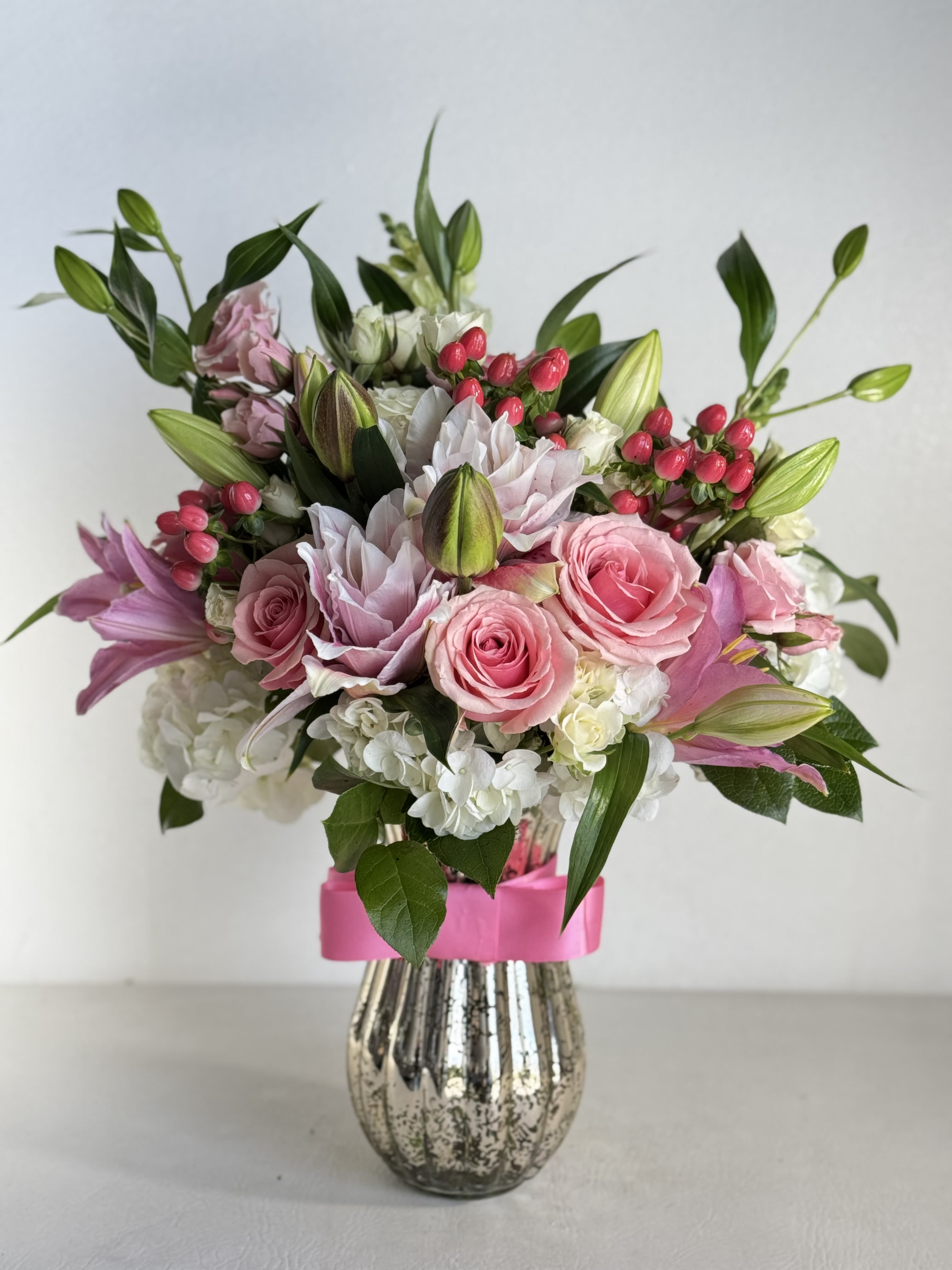 Pink roses and lilies in a silver vase with a pink ribbon