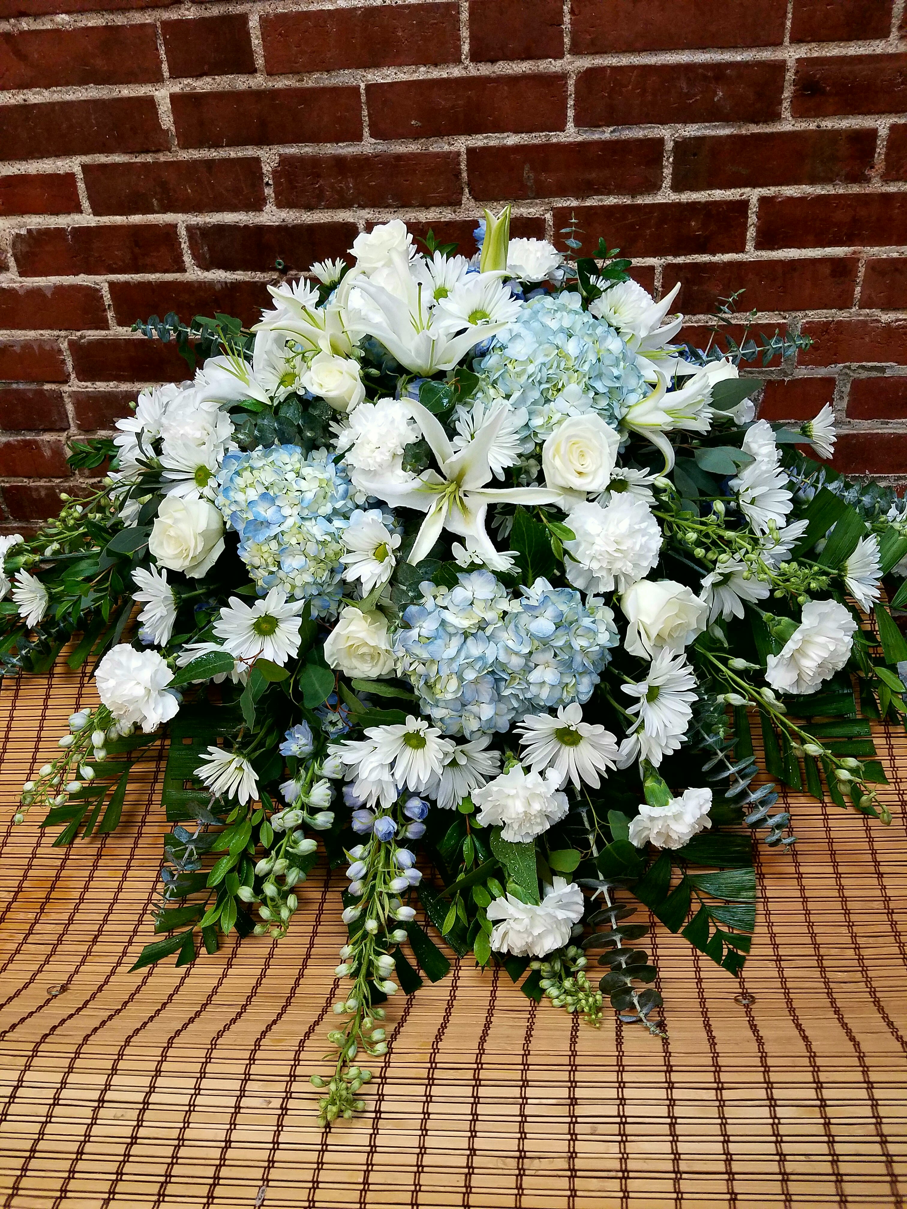 White lilies, roses, daisies, and blue hydrangeas in a low arrangement