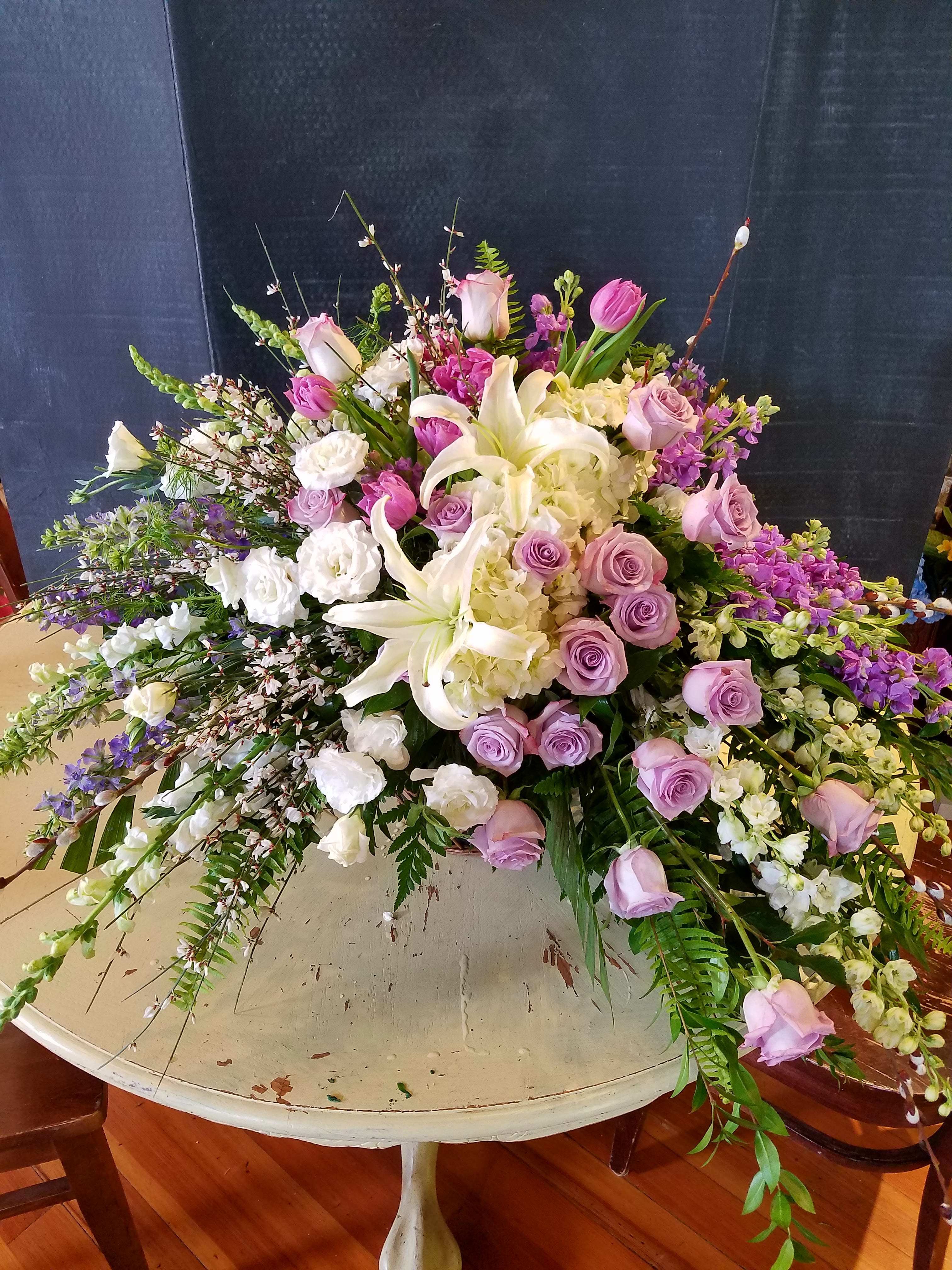 Large pastel floral arrangement with lilies, roses, and hydrangeas on a round table