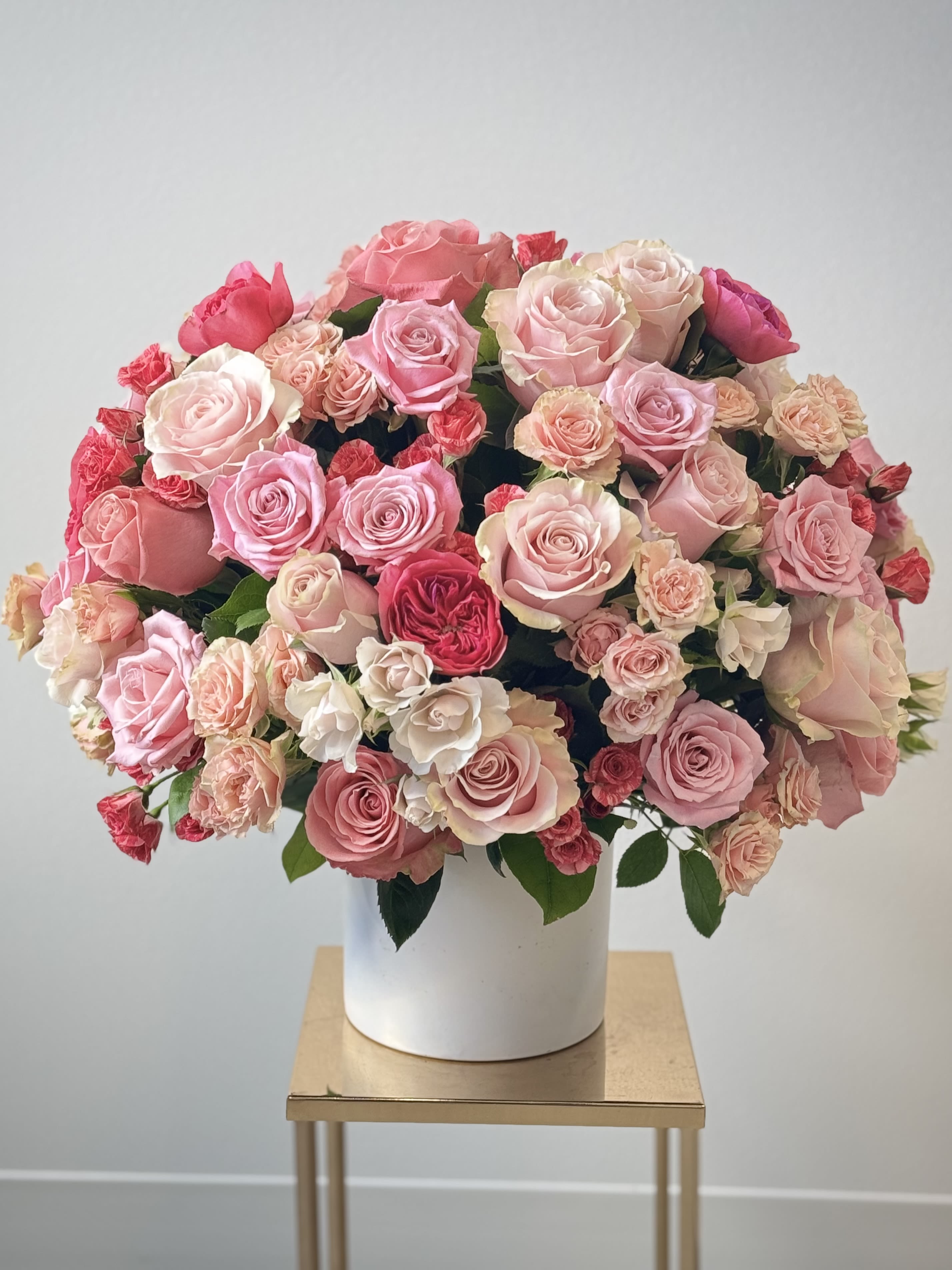 Lovely Romance - Discover the epitome of romance with our "Lovely Romance" luxury rose arrangement – a breathtaking all-around floral masterpiece designed to express deep love and affection. This exquisite romantic rose bouquet features a lavish mix of 70 premium garden roses, classic roses, and delicate spray roses, hand-selected for their vibrant colors and timeless elegance. Expertly arranged in a sophisticated round ceramic vase, the Standard version creates a stunning full, lush display measuring approx. 18x18 in – perfect as a centerpiece or heartfelt gift for anniversaries, Valentine's Day, or any special occasion. Elevate the gesture with our Deluxe option, boasting 100 premium roses for an even more opulent presentation at about 22x22in, ideal for making a grand romantic statement. For ultimate luxury, choose the Premium with 120 roses, forming an impressive 25x25in arrangement. These premium garden roses are sourced for exceptional freshness and longevity, ensuring your flower arrangement remains vibrant. Whether you're searching for the perfect Valentine's Day roses, anniversary flowers, or a luxurious rose bouquet to say "I love you," Lovely Romance captures the essence of true romance in every bloom. This versatile all-around design looks gorgeous from every angle, making it an unforgettable gift for anyone special. Order this premium rose flower arrangement today and let the language of roses speak volumes – a timeless expression of passion, admiration, and heartfelt emotion.