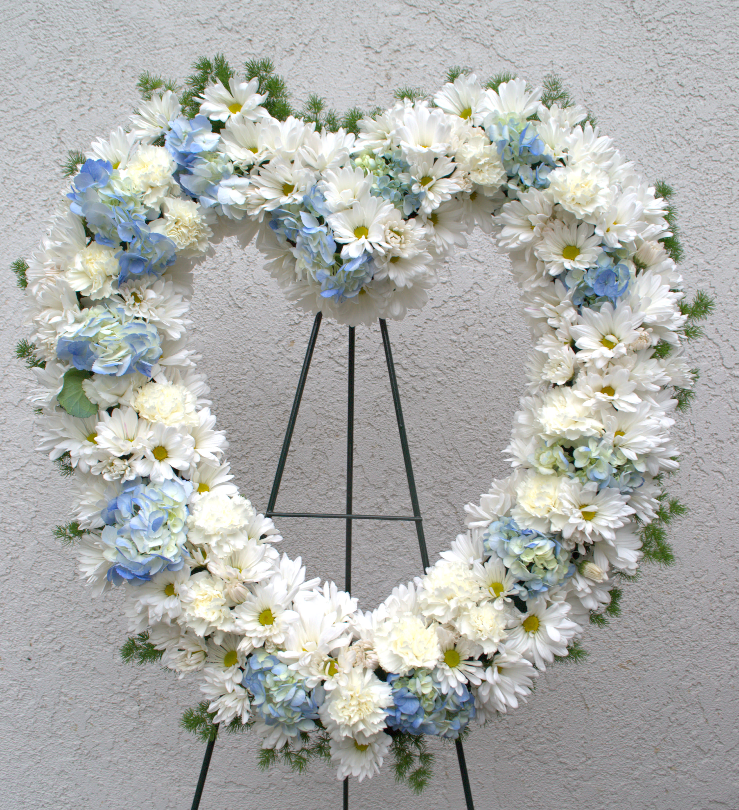 Heart-shaped white and blue floral wreath on a stand