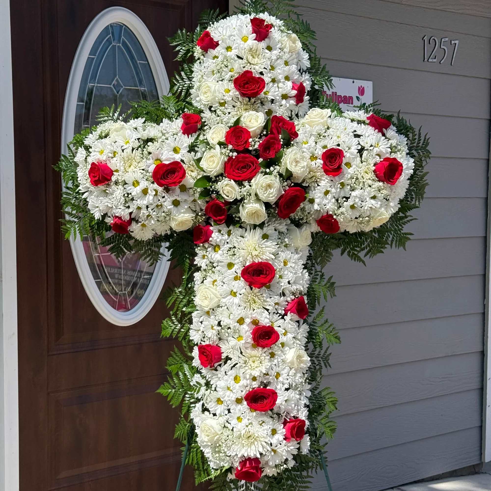 Cruz para funeral - Hermosa cruz floral elaborada con rosas rojas, rosas blancas y delicados crisantemos blancos, acompañada de finos follajes verdes que transmiten paz, amor y respeto. Un arreglo elegante y significativo para honrar la memoria de un ser querido con un detalle lleno de cariño y solemnidad.    Flores frescas de alta calidad  Diseño elegante y artesanal  Ideal para funerales y servicios conmemorativos  Disponible para entrega local  Expresa tus condolencias con una hermosa muestra de amor y respeto.