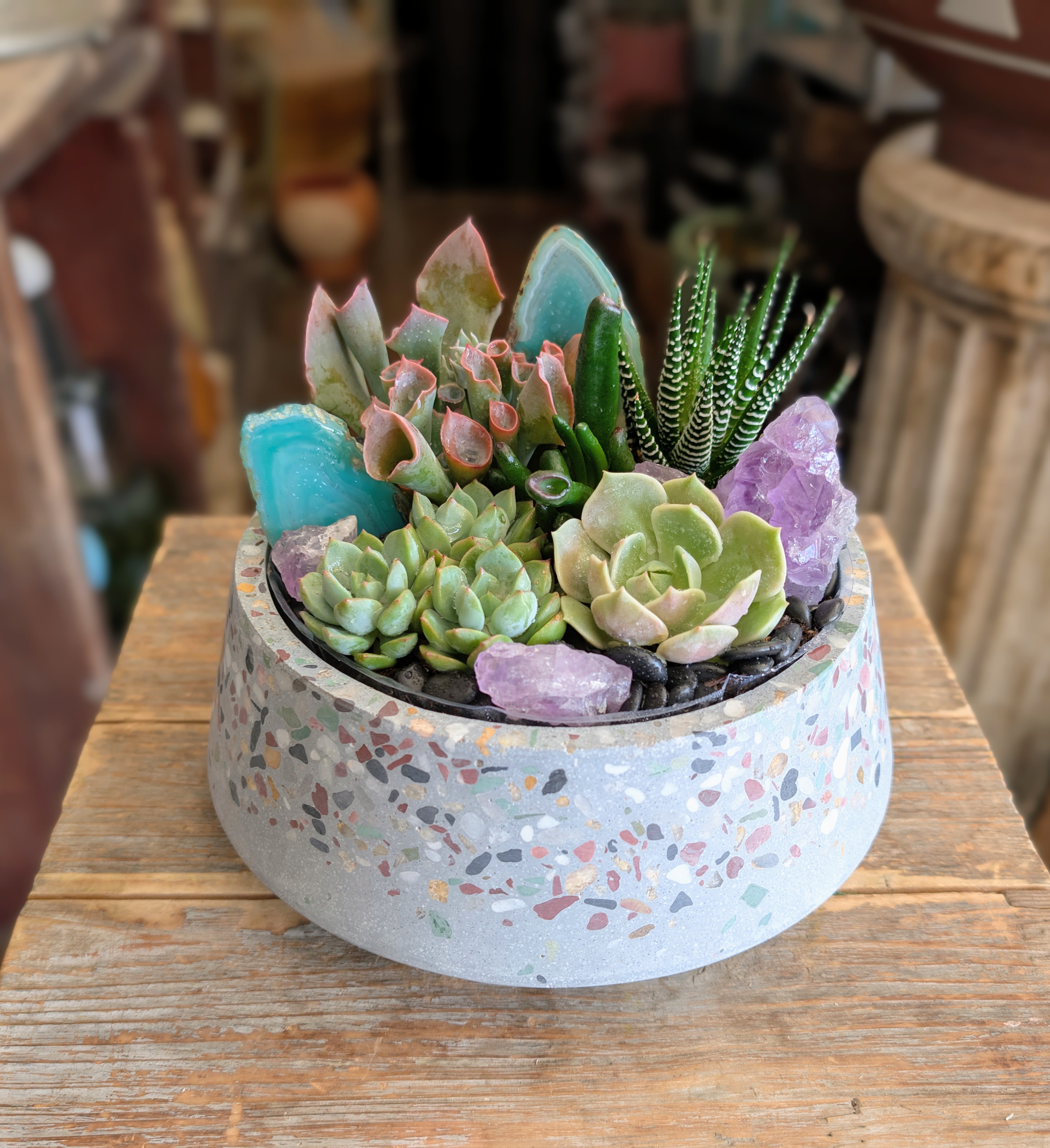 Azura | Crystal Succulent Garden - Inspired by the colors of desert skies, rare minerals, and hidden crystal formations, Azura is a luxurious crystal succulent garden designed as living botanical art by Windmill Floral Expressions. This one-of-a-kind arrangement combines a curated collection of premium succulents with vibrant blue agate slices, natural amethyst, and sculptural textures that create depth, movement, and visual intrigue from every angle.Designed in a modern terrazzo vessel, Azura blends the beauty of living plants with the organic elegance of natural stone. Soft rosettes, architectural succulents, and crystal accents come together to create a miniature landscape that feels both contemporary and timeless. As part of the signature collection from Windmill Floral Expressions, this luxury succulent garden is thoughtfully handcrafted to elevate any home, office, or interior space.  Perfect as a thoughtful gift or a striking accent for home or office décor, Azura offers a long-lasting al Available for local delivery in Las Vegas and Henderson, Azura is part of our Luxe Succulent Gardens collection and makes a memorable gift for birthdays, housewarmings, thank-you occasions, corporate gifting, sympathy gifts, and anyone who appreciates distinctive botanical design. Whether you're searching for a luxury plant gift, a unique succulent arrangement, or an artistic alternative to fresh flowers, Windmill Floral Expressions delivers exceptional botanical creations throughout the Las Vegas Valley.
