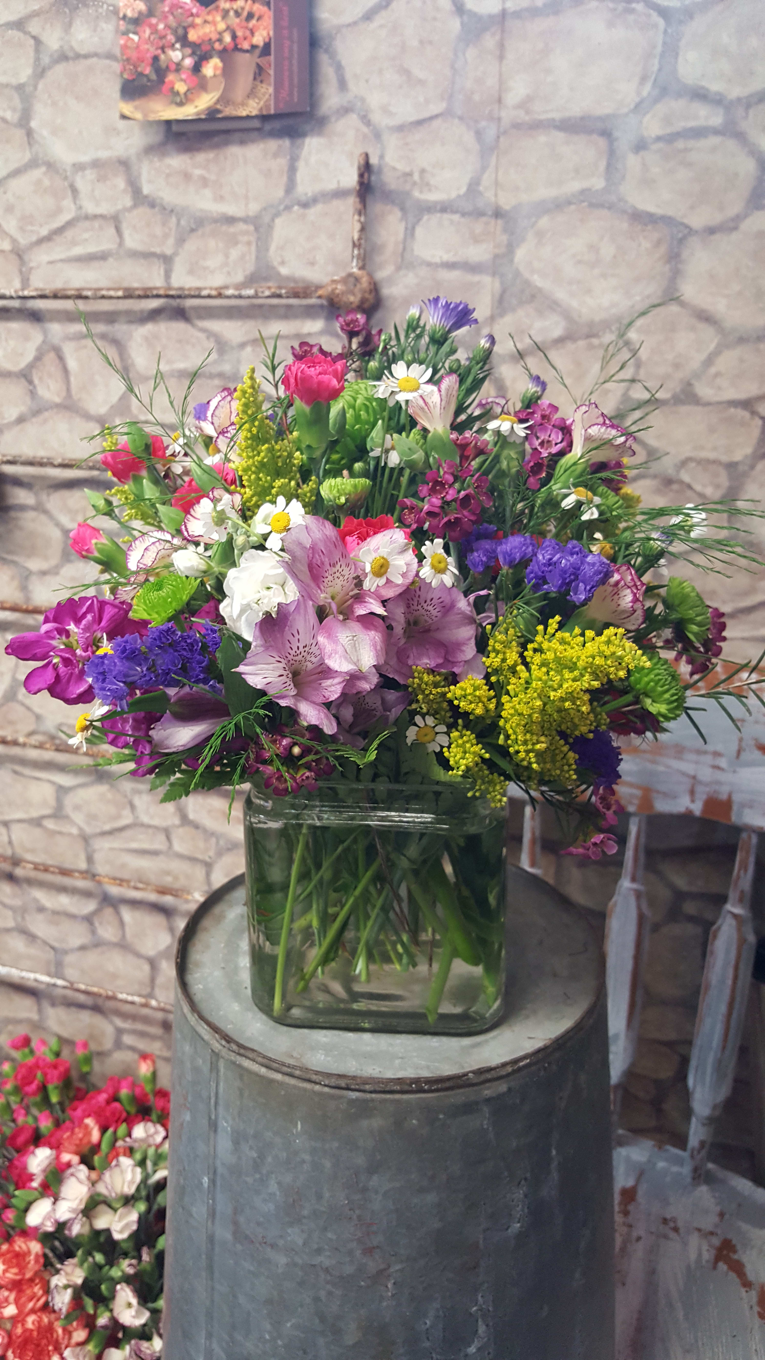 Mixed bouquet of pink, purple, white, and yellow flowers in a glass vase