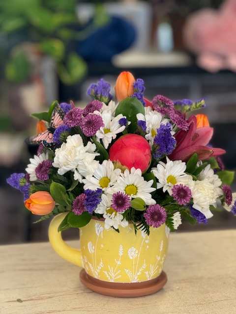 Mixed bouquet in a yellow mug with white daisies, purple blooms, and orange tulips