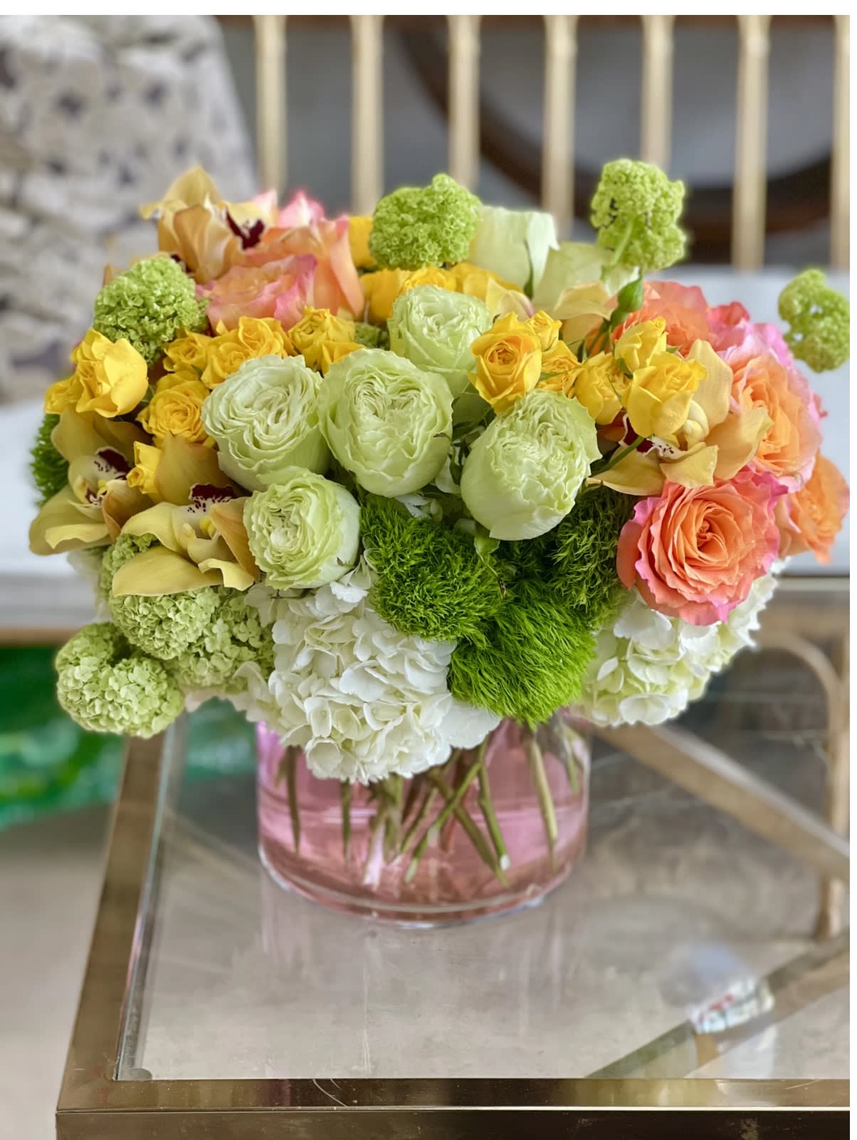 Bouquet of yellow, peach, and green flowers in a pink glass vase