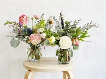 Two mixed flower arrangements in clear glass vases on a stool