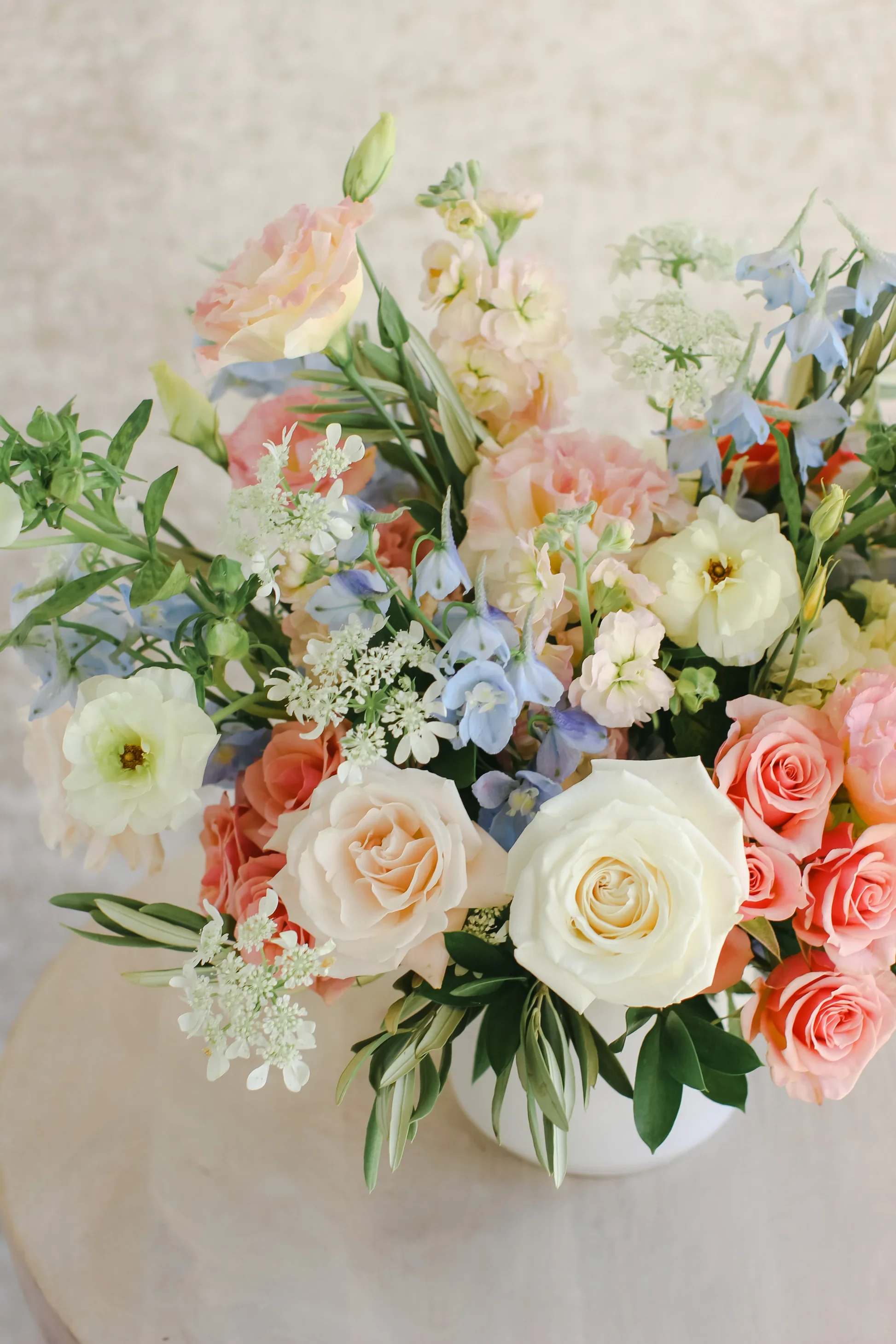 Pastel bouquet of roses, blue flowers, and white blooms in a white vase