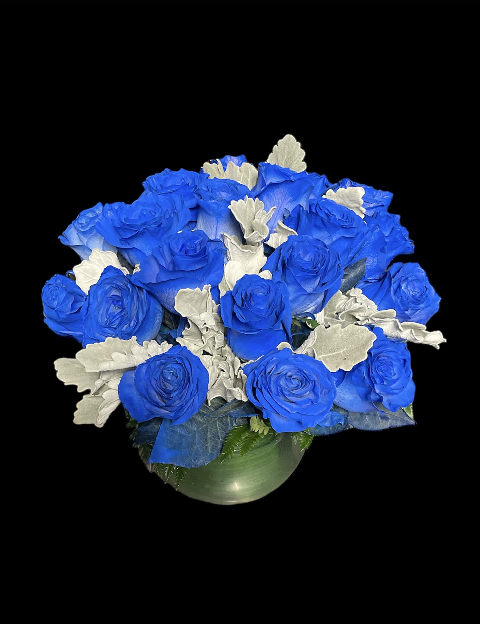 Blue roses arranged in a round vase with silver foliage