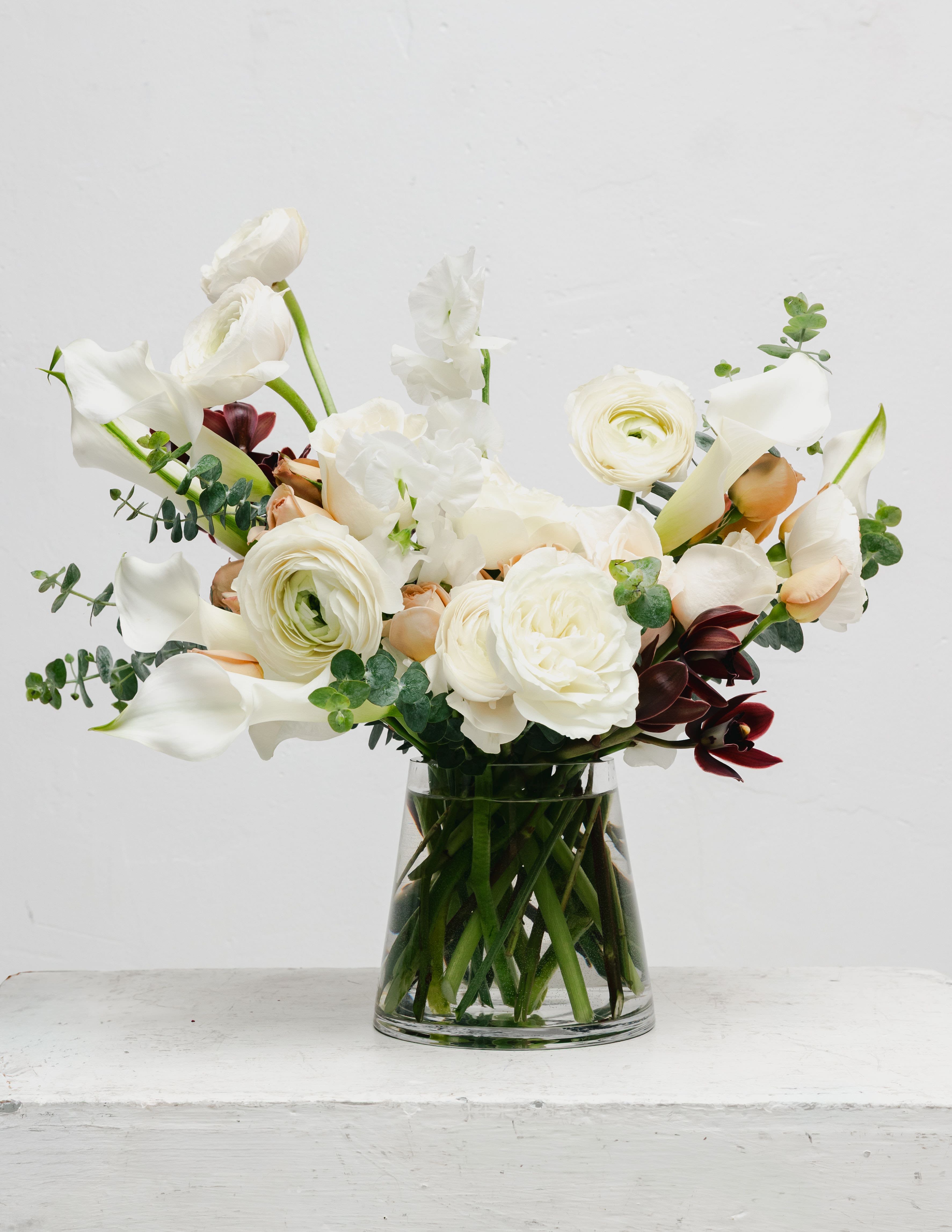 White floral arrangement in a clear glass vase with calla lilies and ranunculus
