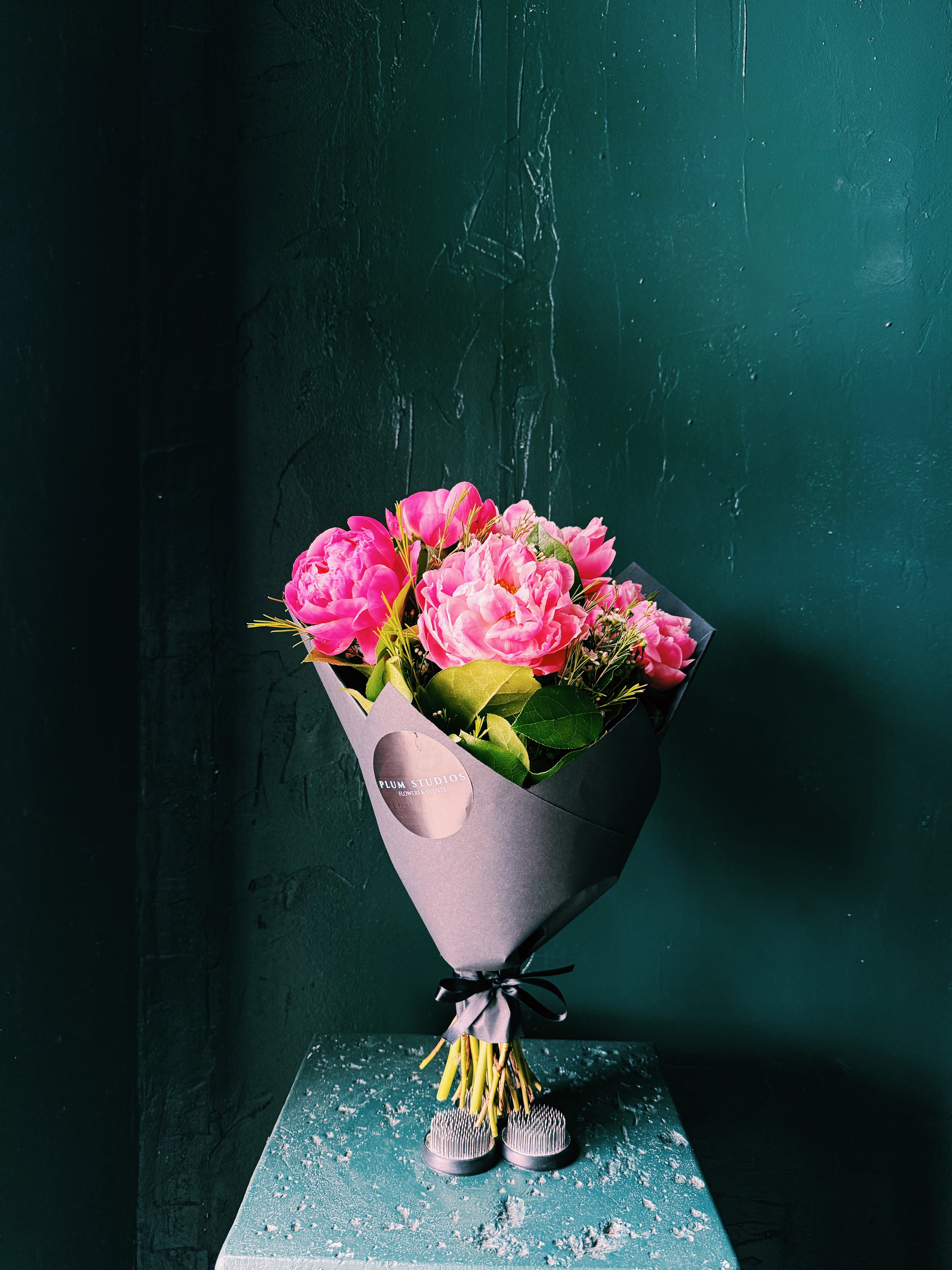 Pink peony bouquet wrapped in dark paper with a black ribbon