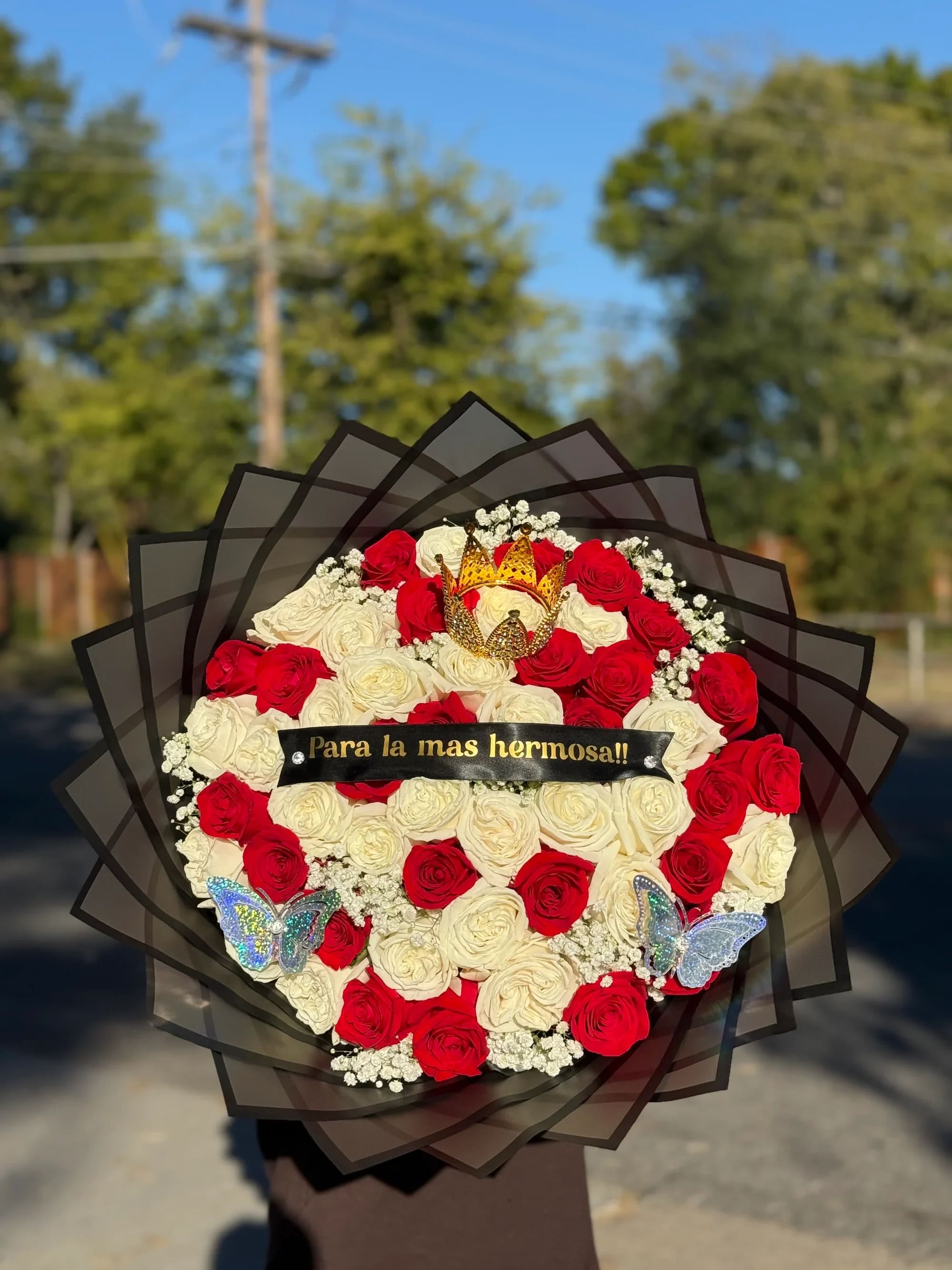 Ramo buchon 10 - Ramo “Para la Más Hermosa” – Rosas Premium con Corona y Mariposas  Sorprende a esa persona especial con este elegante arreglo de rosas rojas y blancas, diseñado para expresar amor, admiración y ternura en cada detalle.   Este hermoso bouquet incluye:  • Rosas rojas y blancas frescas de alta calidad  • Delicados detalles de flores blancas decorativas  • Corona decorativa dorada que le da un toque real   • Mariposas brillantes que resaltan su belleza  • Listón con mensaje especial: “Para la más hermosa”  • Envoltura elegante en papel negro estilo coreano   Perfecto para cumpleaños, aniversarios, San Valentín o simplemente para recordarle que es la reina de tu corazón.    Un regalo inolvidable que combina romanticismo, elegancia y exclusividad.  Si quieres también te puedo hacer una versión más corta o más elegante para tu tienda.