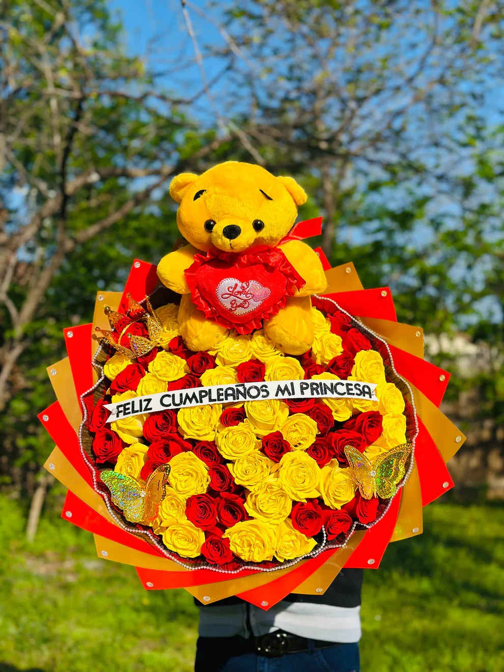 Ramo buchon 22 - Sorprende en su día especial con este hermoso y elegante arreglo floral en forma de corazón, elaborado con rosas rojas y amarillas de alta calidad. Un diseño vibrante que combina pasión, alegría y amor en cada detalle.  Incluye:   Rosas rojas y amarillas frescas  Delicados detalles de flor blanca (baby’s breath)  Moño decorativo elegante  Hermosas mariposas decorativas  Banda personalizada con el mensaje “Feliz cumpleaños bonita”  Perfecto para cumpleaños, aniversarios o para expresar amor y admiración de una manera inolvidable. Su presentación moderna y sofisticada lo convierte en el regalo ideal para sorprender y enamorar.   Disponible para entrega especial.  Producto elaborado con flores frescas y diseño artesanal.
