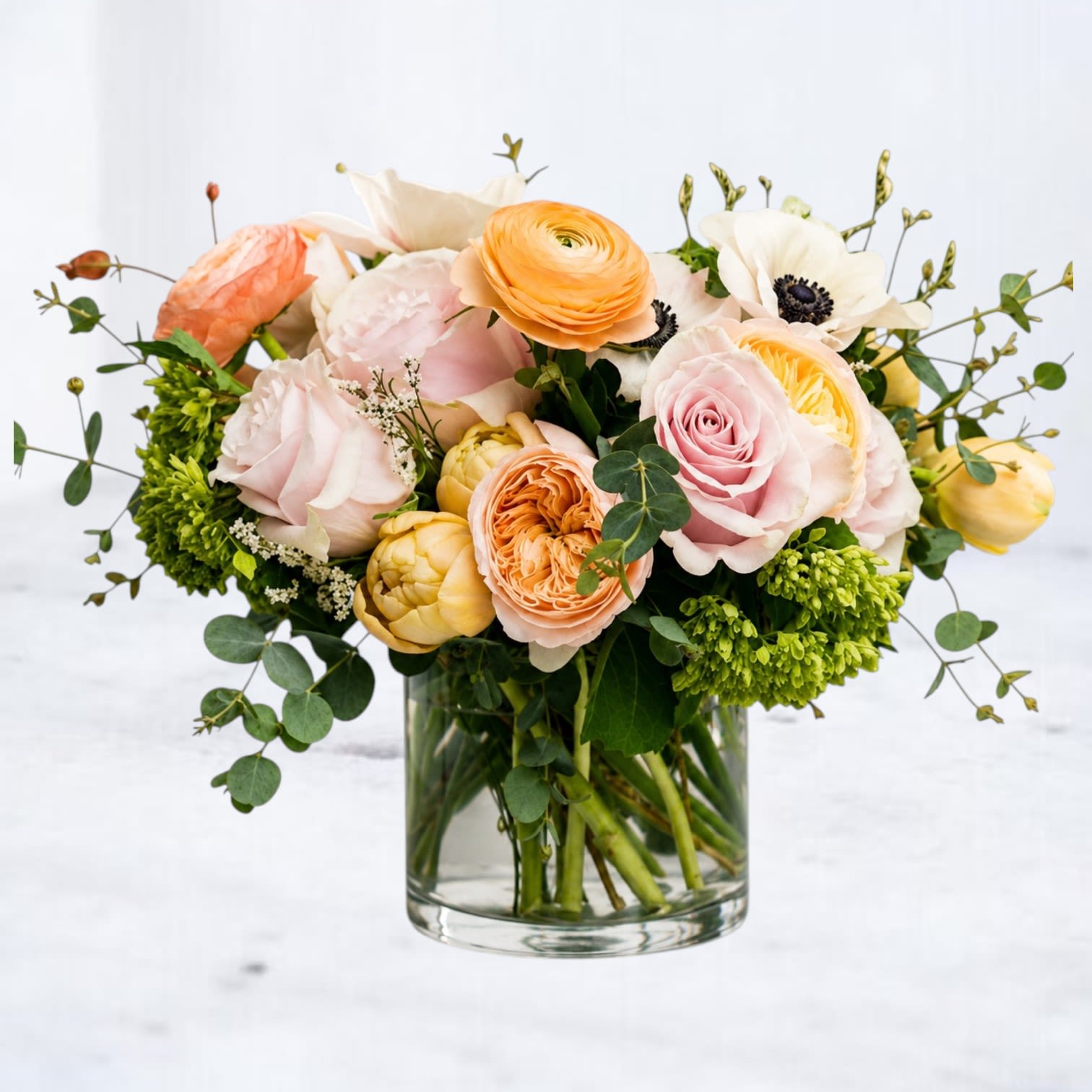 Elysian Bloomscape - Graceful and garden-forward, Elysian Bloomscape captures the beauty of soft color, natural movement, and abundant texture. A harmonious blend of blush, ivory, and fresh greenery creates a full, flowing arrangement with a relaxed yet elevated feel.  Designed with premium seasonal flowers and a generous hand, this piece offers the look of a lush garden gathering—perfect for everyday celebrations, heartfelt thanks, or simply brightening someone’s space.  Flower varieties may vary based on seasonal availability, but overall color palette, style, and fullness will be thoughtfully maintained.