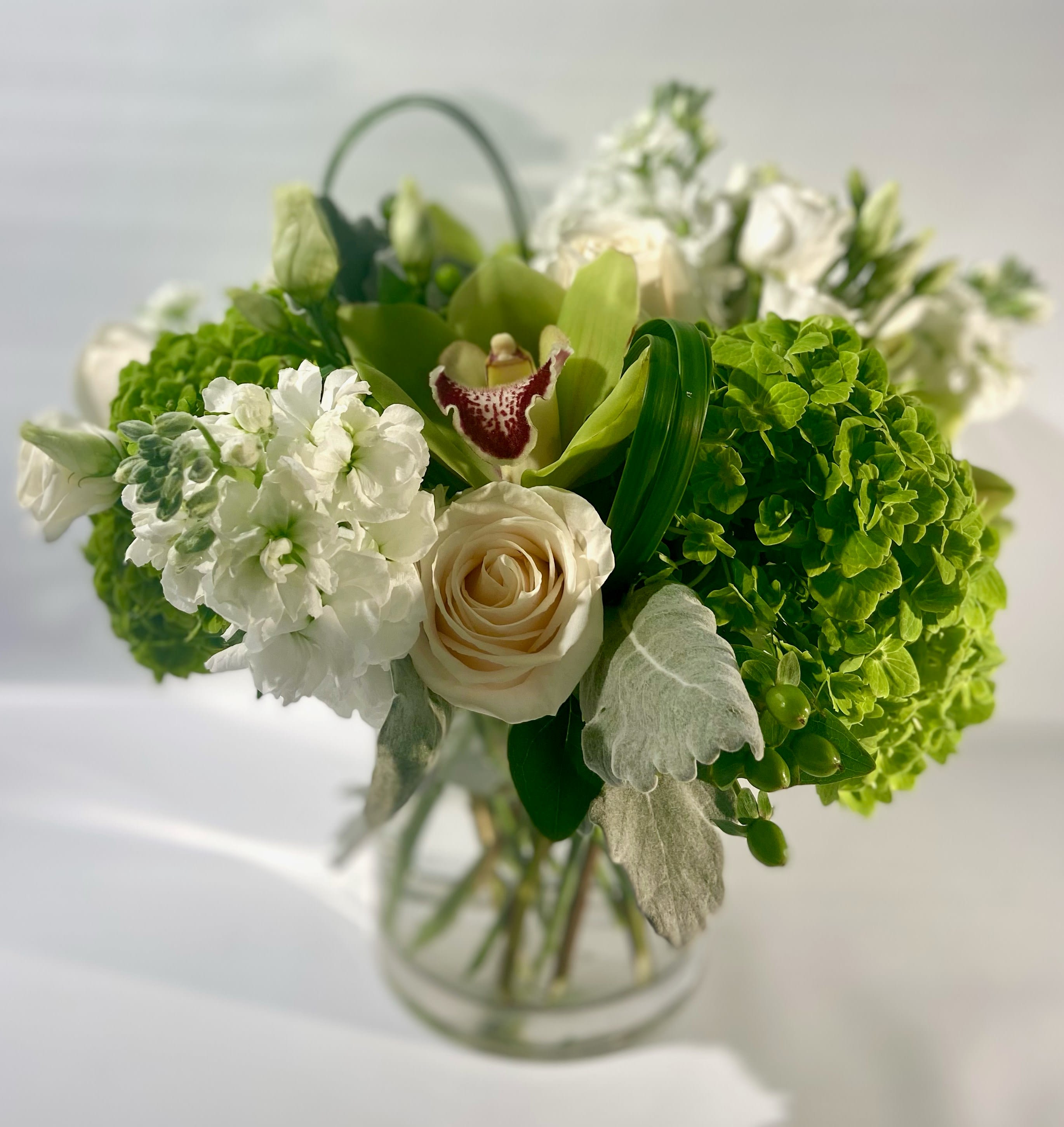 Green and white bouquet with roses and orchids in a glass vase