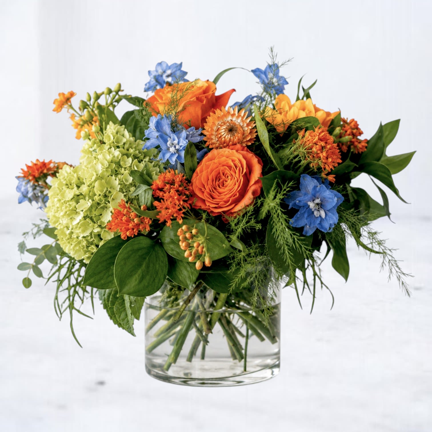 Orange and blue mixed flower arrangement in a clear glass vase