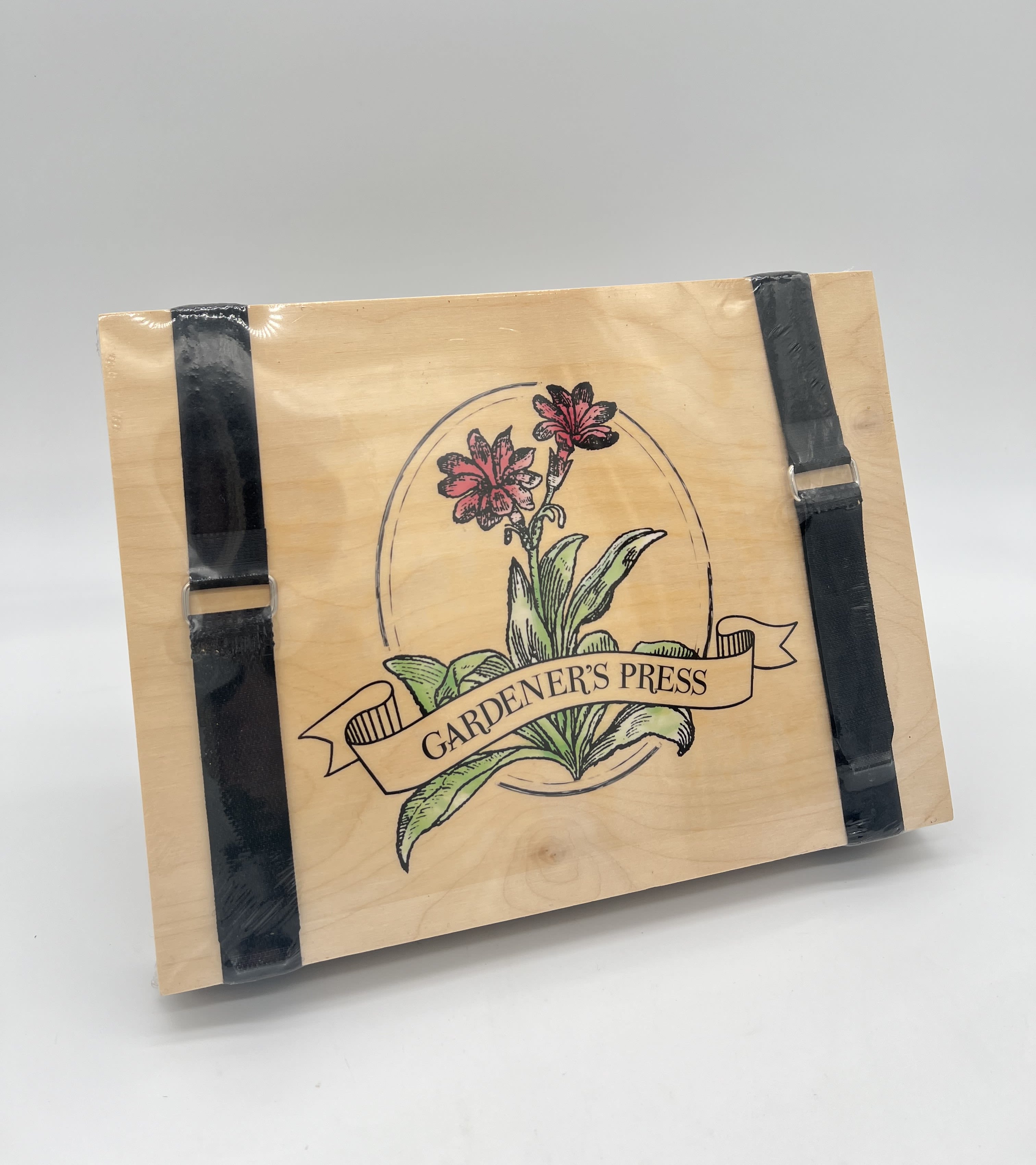 Wooden gardener’s press with floral illustration and two black straps