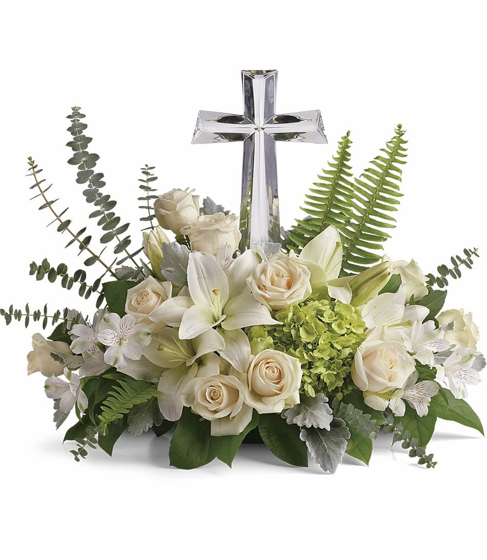 Low arrangement of white lilies and roses with green hydrangea and a clear crystal cross in the center
