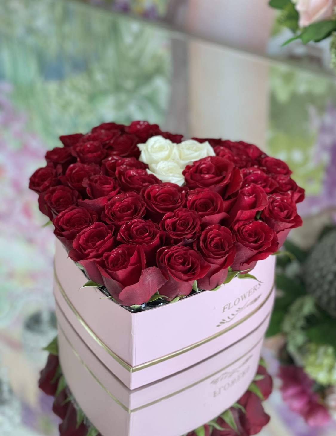 LARGE HEART BOX 50 FRESH ROSES - A bold heart-shaped display of 50 fresh roses makes an unforgettable anniversary or love-and-romance gift that will make her feel truly cherished. This LARGE HEART BOX 50 FRESH ROSES reads like a classic declaration-deep red roses packed tightly into a decorative heart box, accented with small clusters of white roses and gold-wrapped chocolates for a touch of luxury. It's also perfect for birthdays or a "just because" surprise when you want the person you love to feel seen and celebrated.  Each arrangement is arranged in a pale pink or red heart-shaped presentation box with subtle gold trim, creating a compact, polished look that's easy to place on a table, desk, or bedside. The mix of rich red petals and bright white contrast draws the eye while the chocolates tucked among the blooms add an indulgent, gift-box feel. Order this floral heart to mark anniversaries, Valentine's Day, birthdays, or an everyday romantic moment - sized to impress without overwhelming the space and crafted to keep the roses looking fresh as long as possible with basic care: keep water filled in the box reservoir and avoid direct sun or heat.