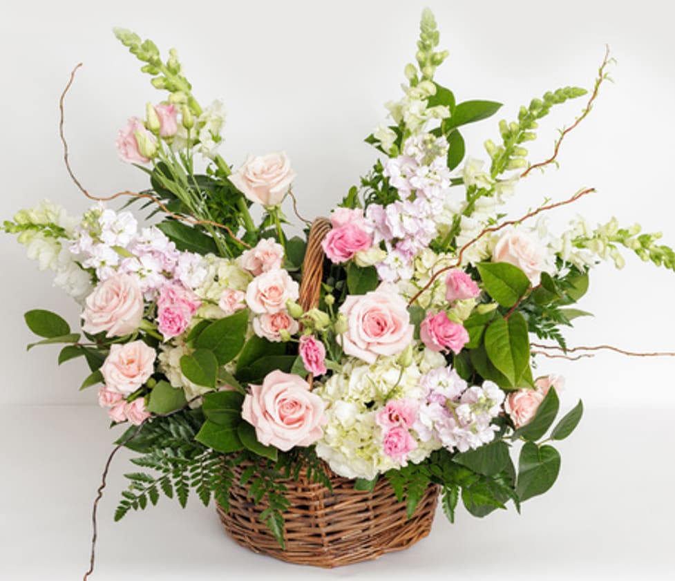 Pastel pink and white flower basket with roses, snapdragons, and other blooms in a woven wicker basket