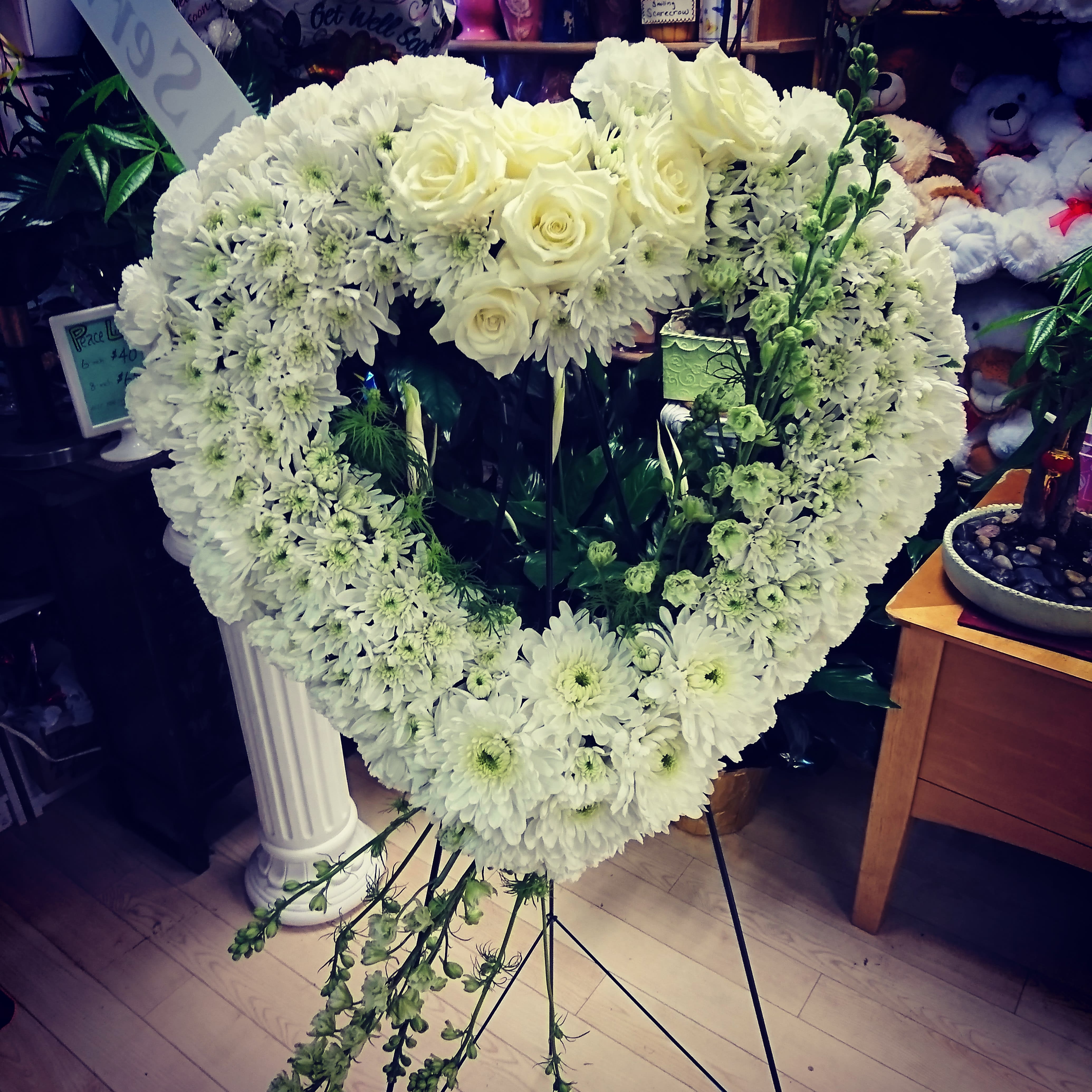 Heavenly Heart Spray  - A beautiful heart is a wonderful way to share your thoughts of condolences and sympathy. It's all-white designed with roses, cushion chrysanthemums, and larkspur angelic wings. Approximately 20" wide x 20" tall. 